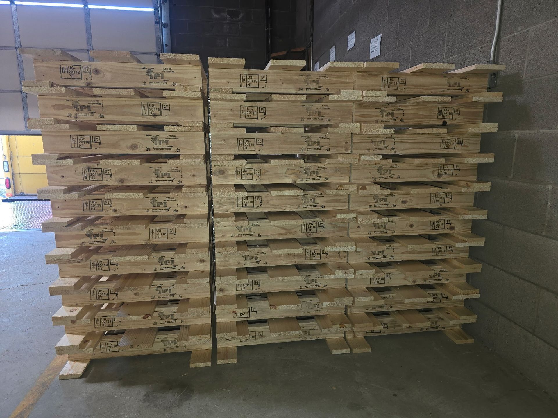 Stacks of wooden pallets piled in a warehouse beside a loading dock door