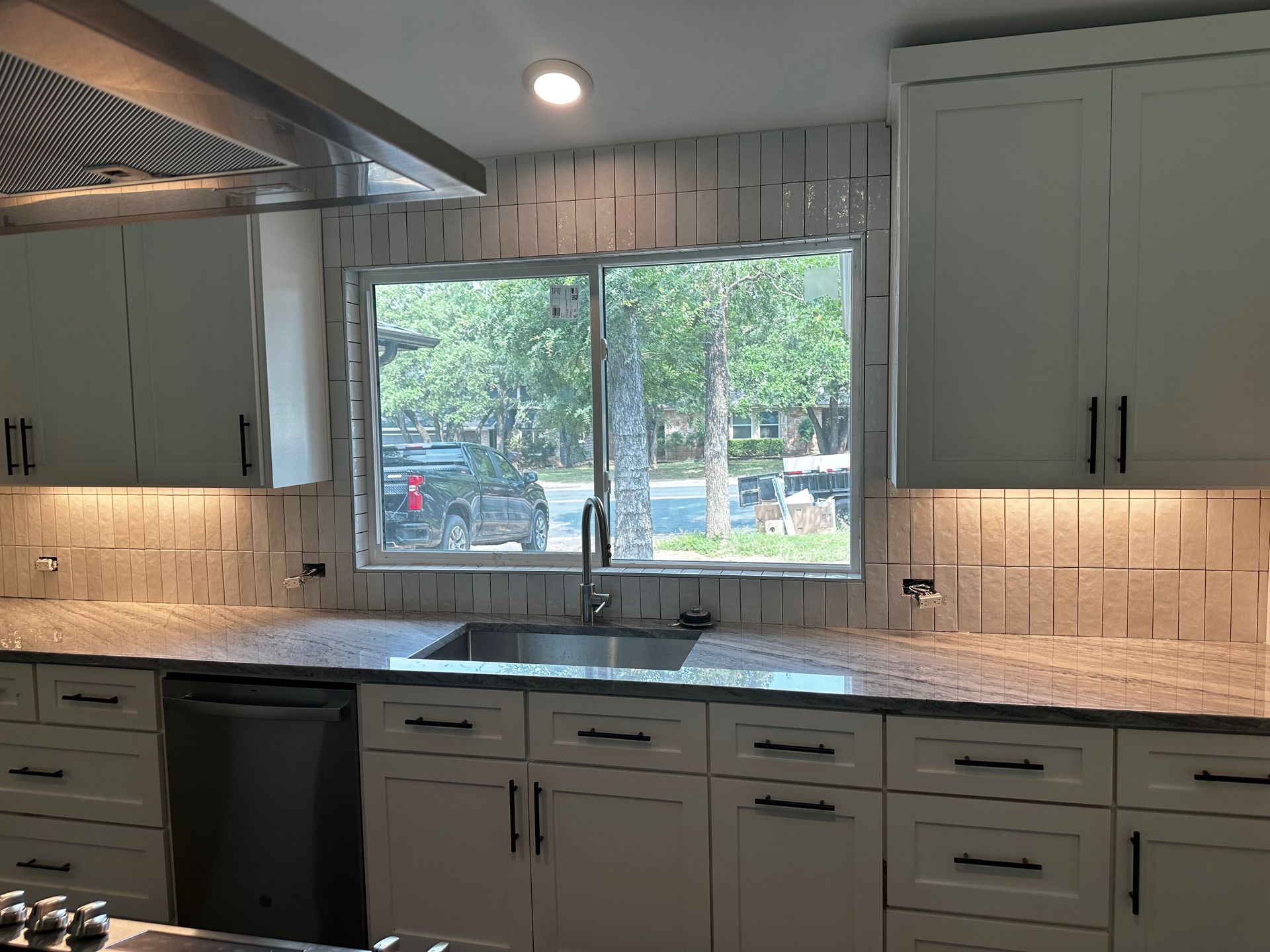 A kitchen with white cabinets, granite counter tops, a sink, and a window.