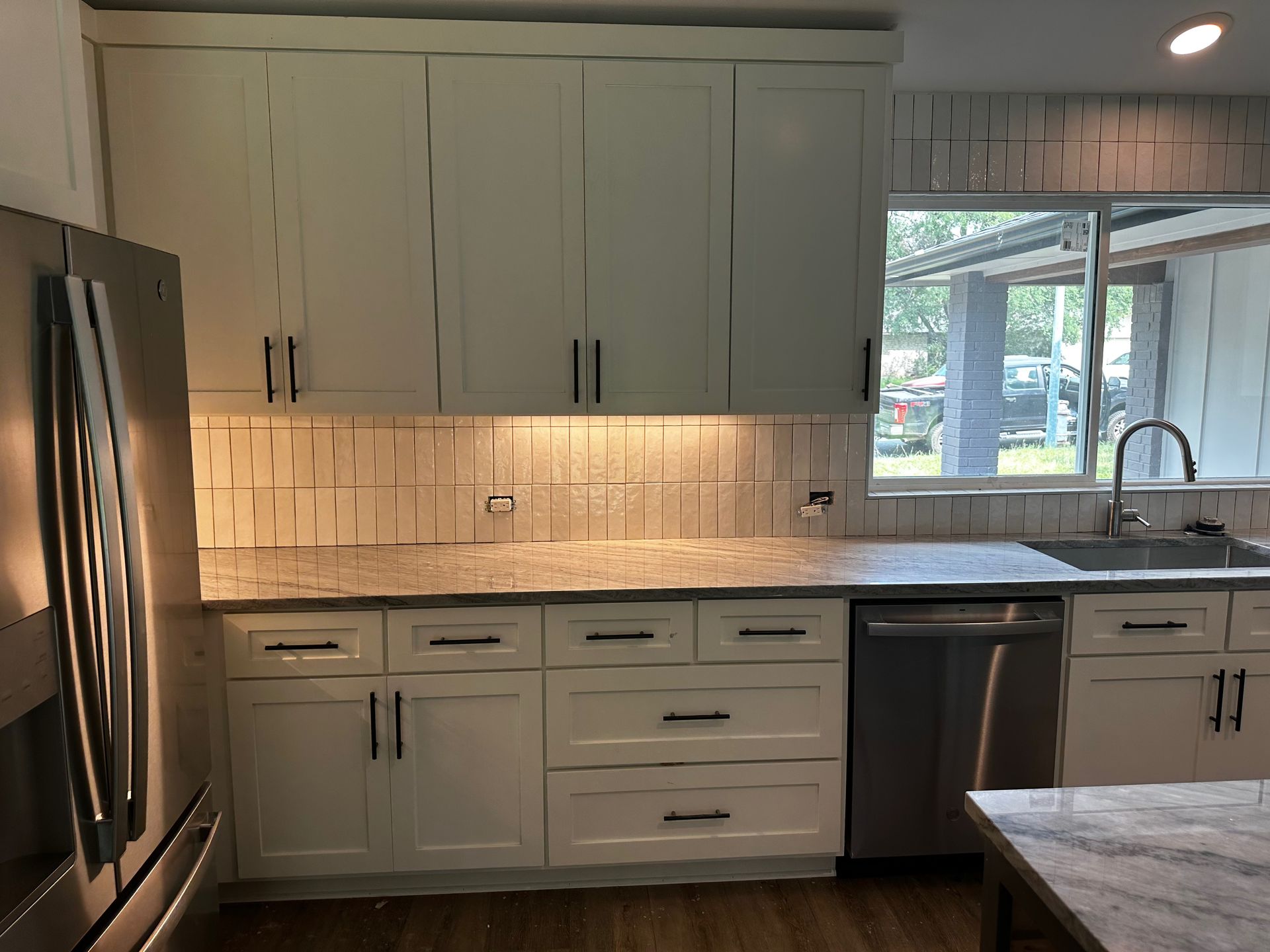 A kitchen with white cabinets, stainless steel appliances, a sink, and a window.