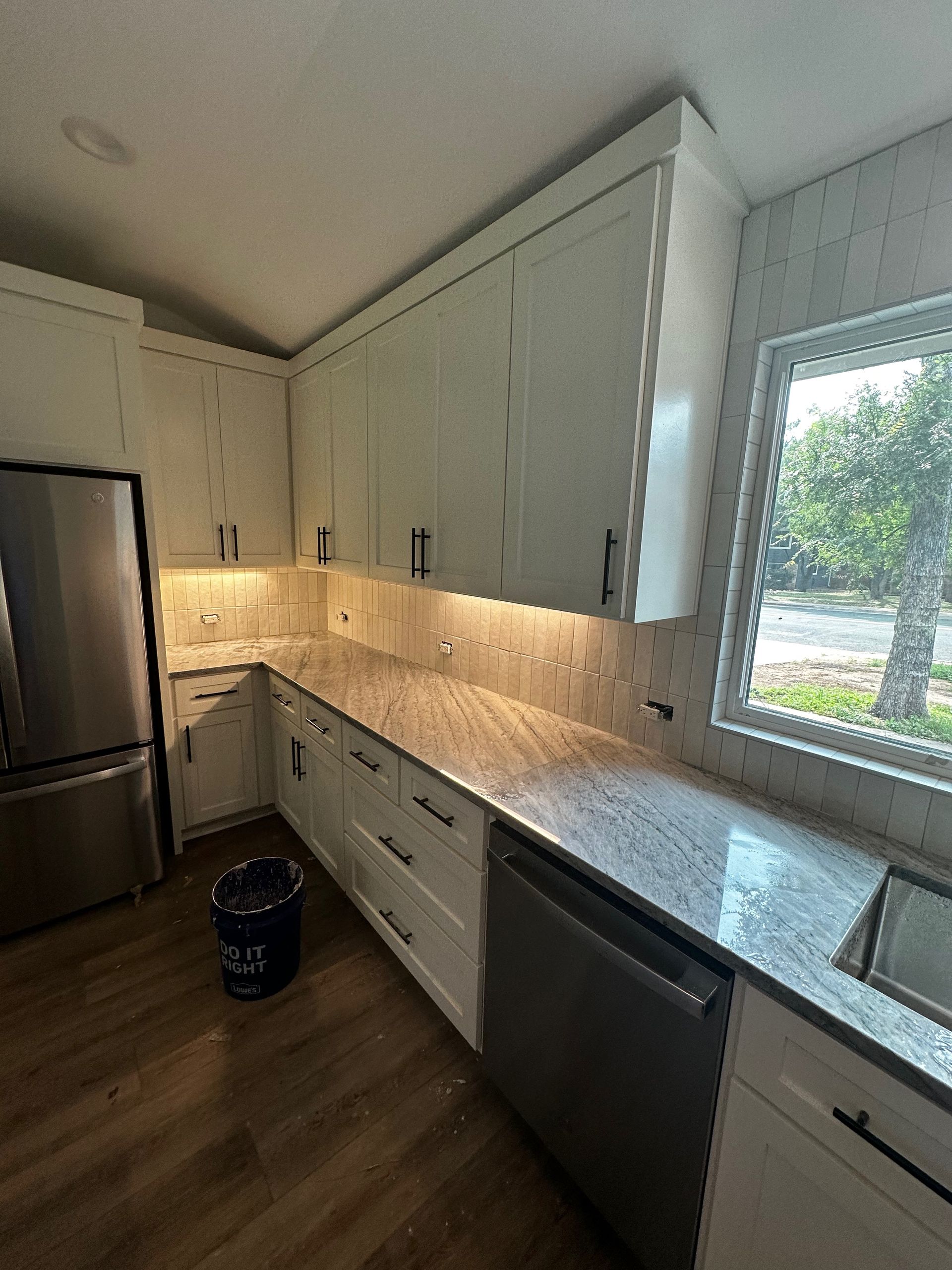 A kitchen with white cabinets, granite counter tops, stainless steel appliances, and a window.