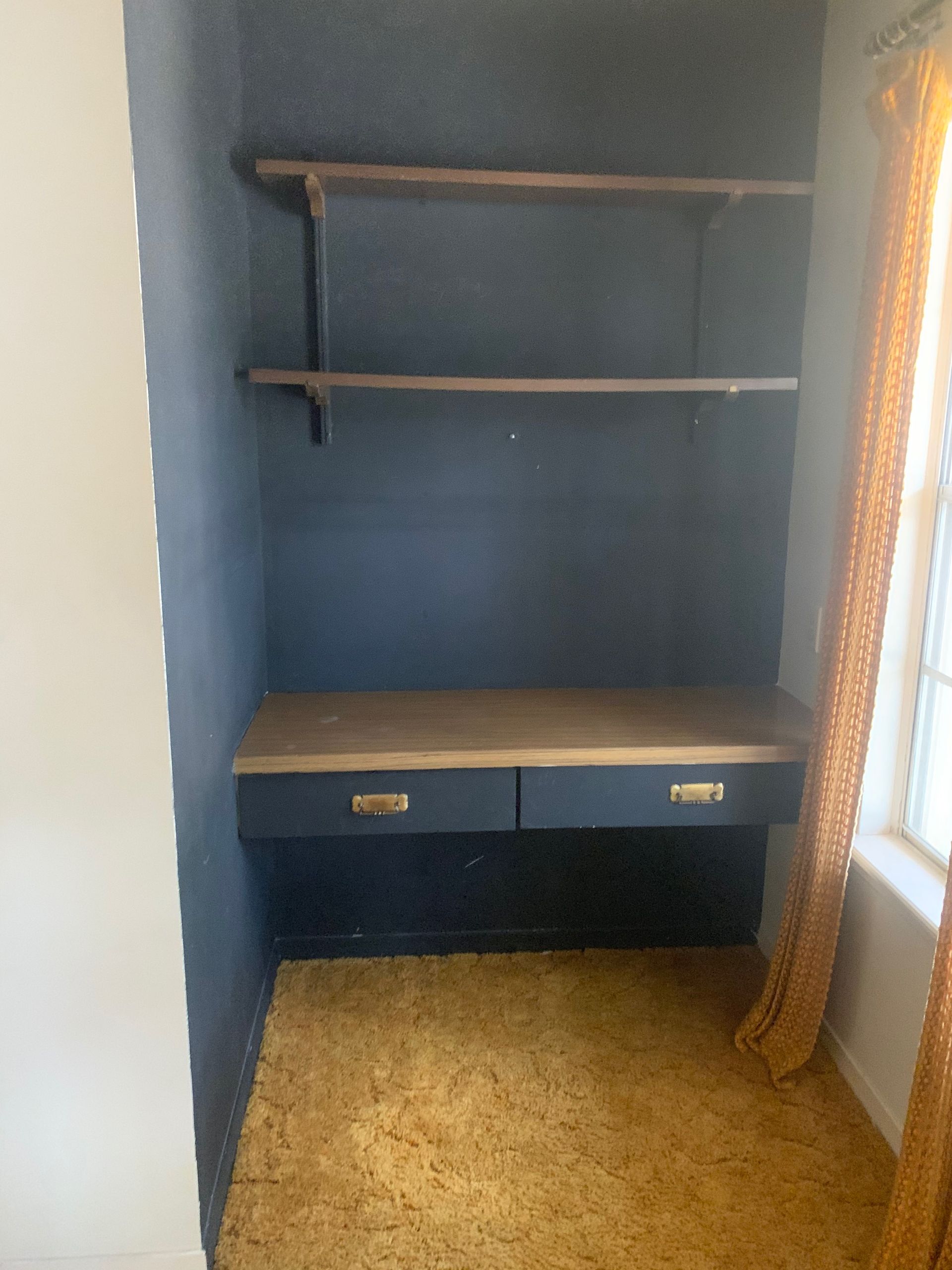 An empty room with a desk and shelves and a window.