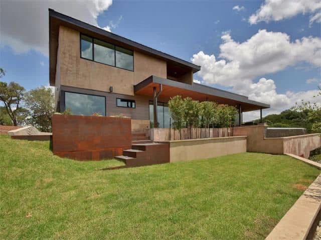 A large house with a lot of windows is sitting on top of a lush green hillside.