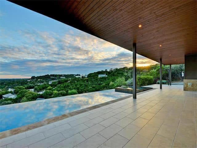 A large patio with a view of a lush green hillside and a swimming pool.