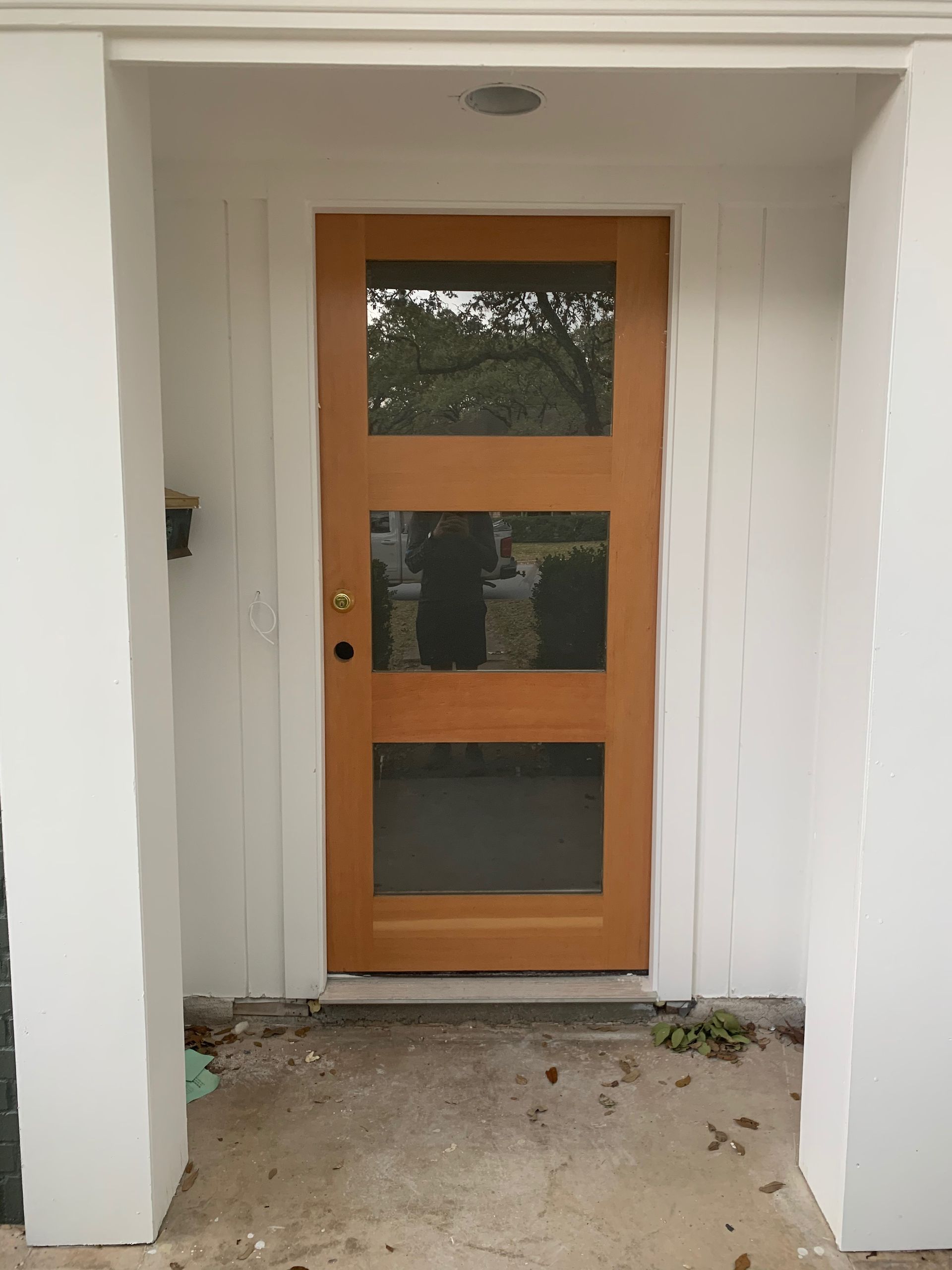 A wooden door with three windows on a white wall.