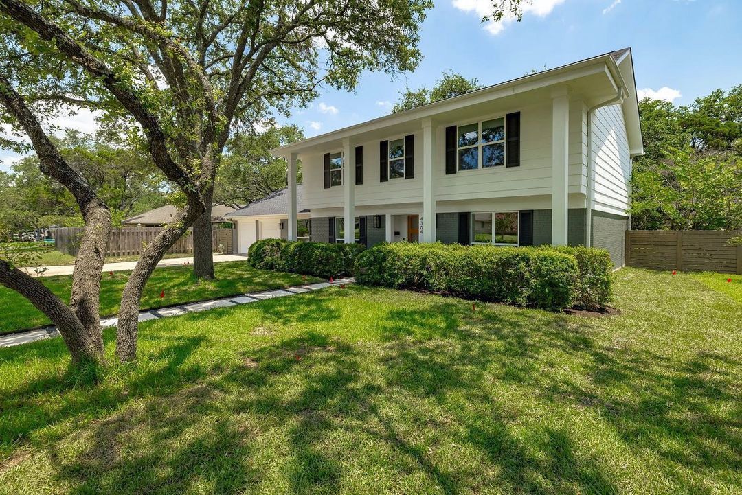 A large white house with a lush green lawn and trees in front of it.
