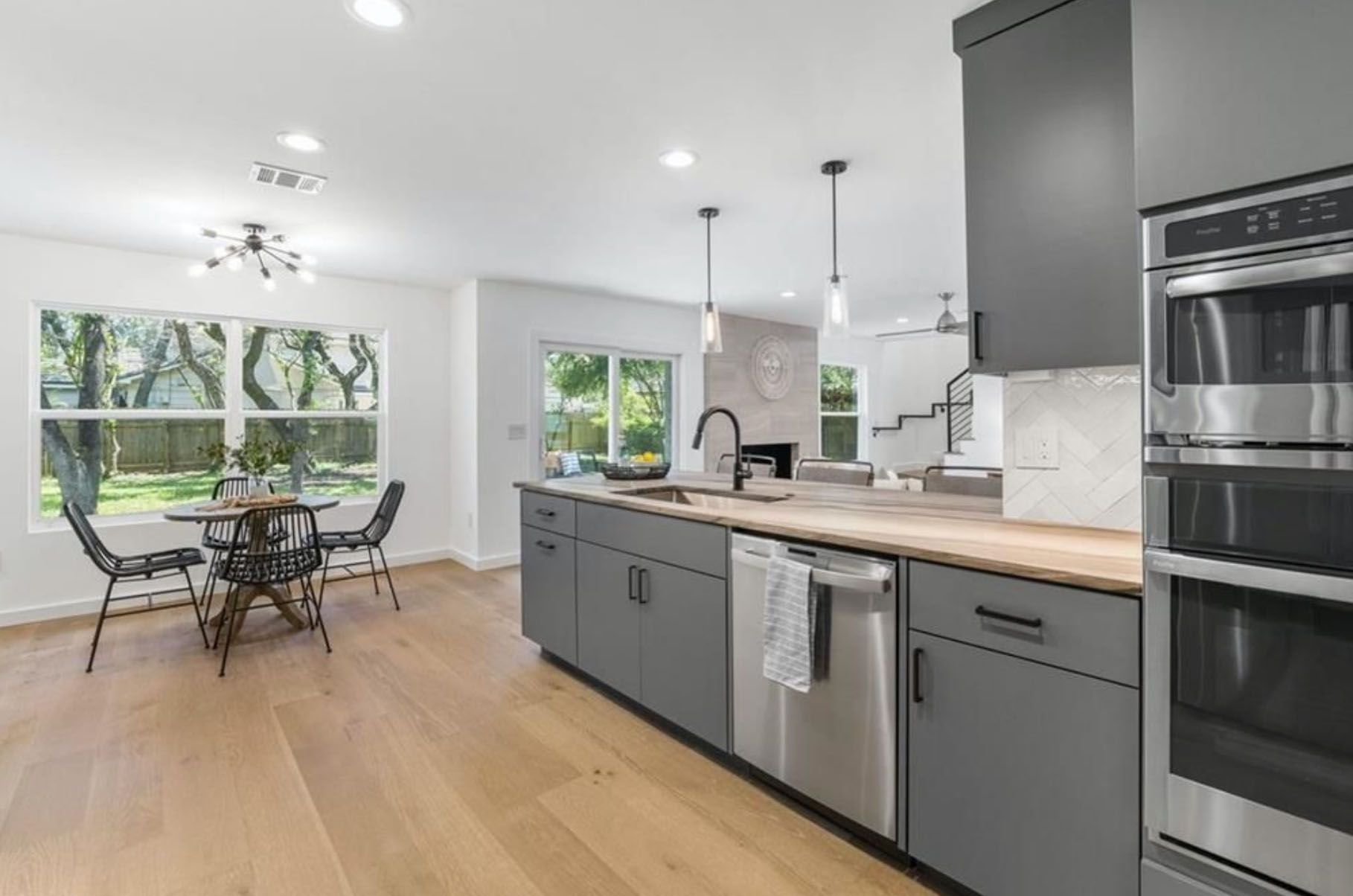 A kitchen with gray cabinets and stainless steel appliances and a dining room in the background.