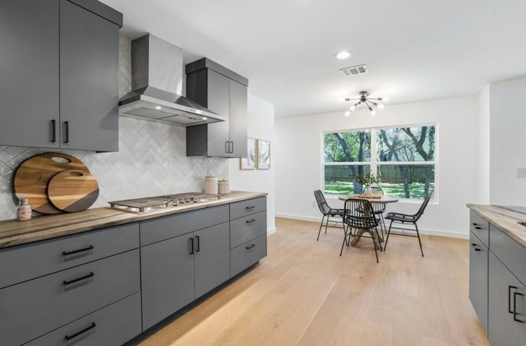 A kitchen with gray cabinets, a stove, a table and chairs.