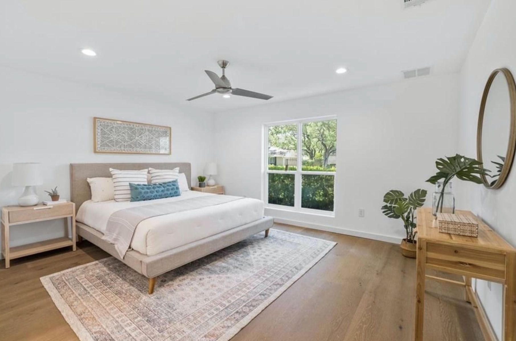 A bedroom with a bed, nightstand, mirror and ceiling fan.