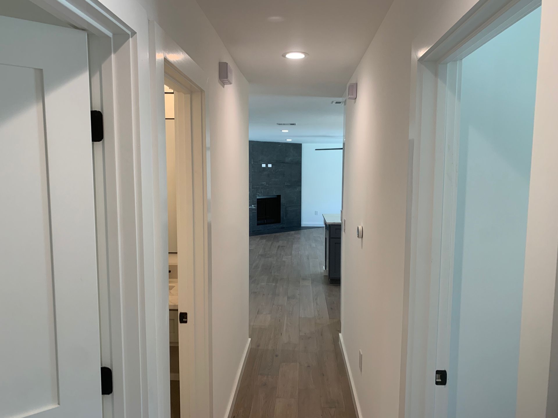 A long hallway with white walls and hardwood floors leading to a living room.