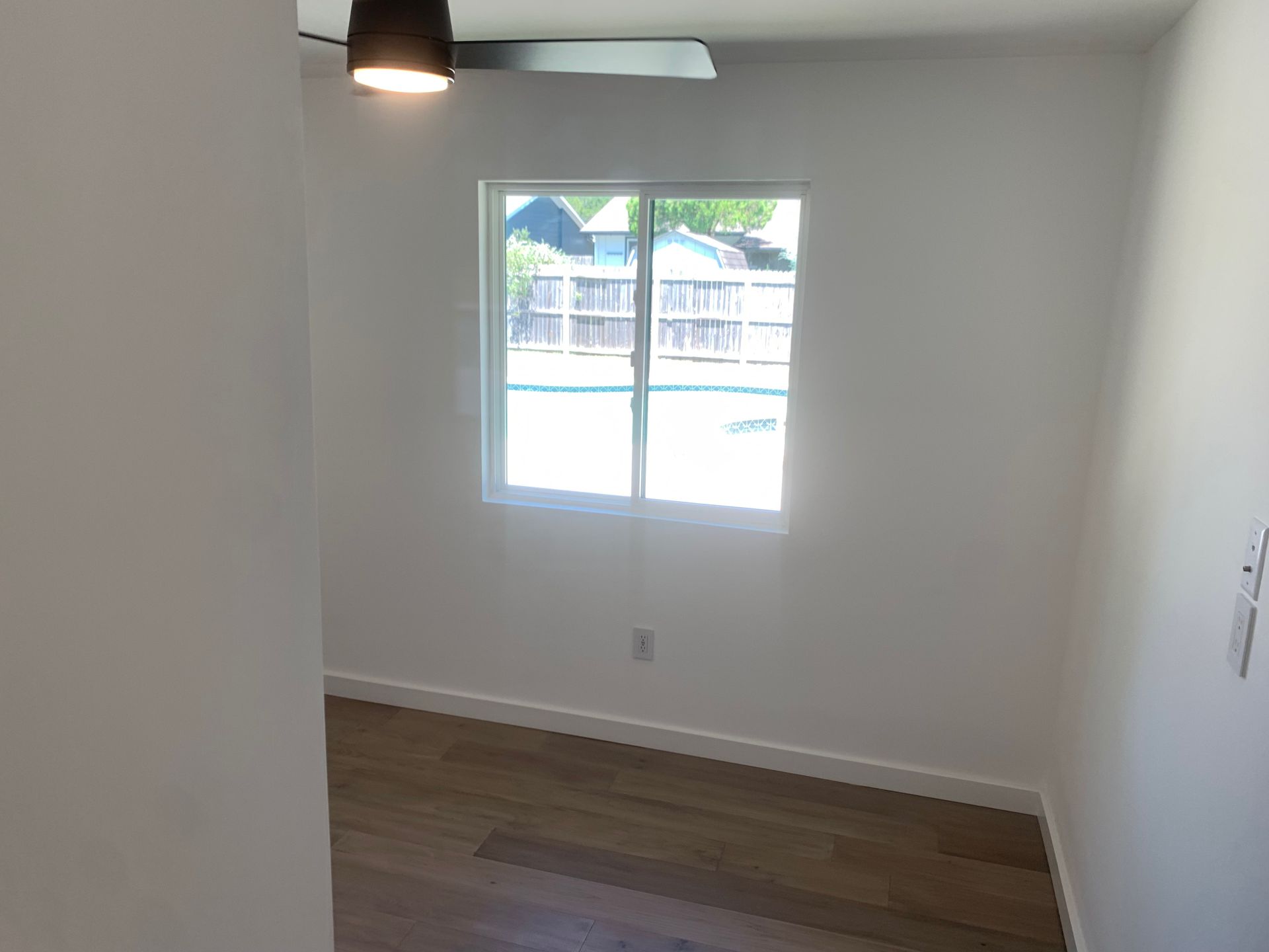 An empty room with a window and a ceiling fan.