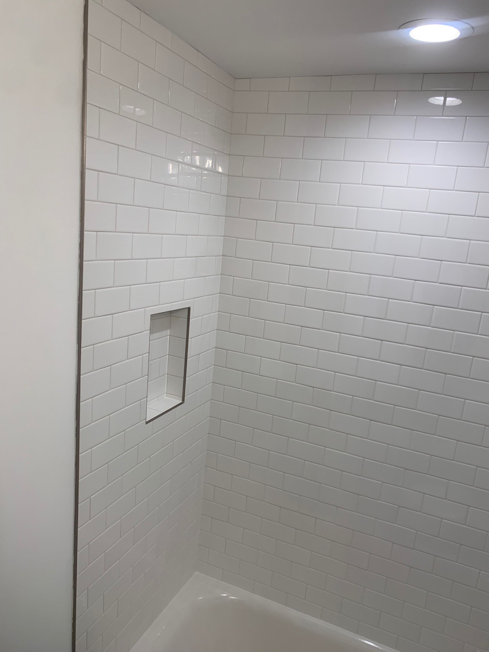 A bathroom with white tile walls and a bathtub.