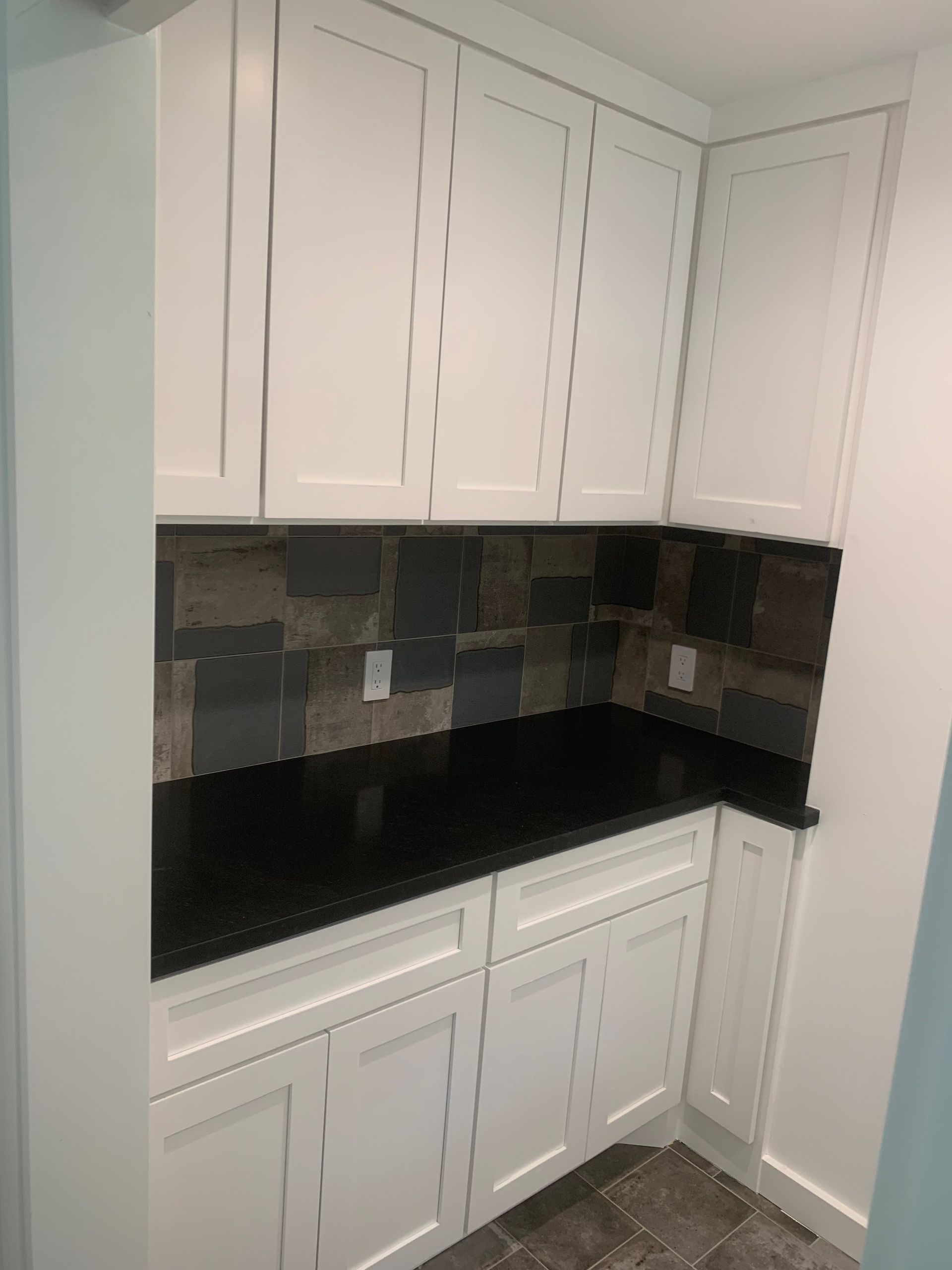 A kitchen with white cabinets and black counter tops.