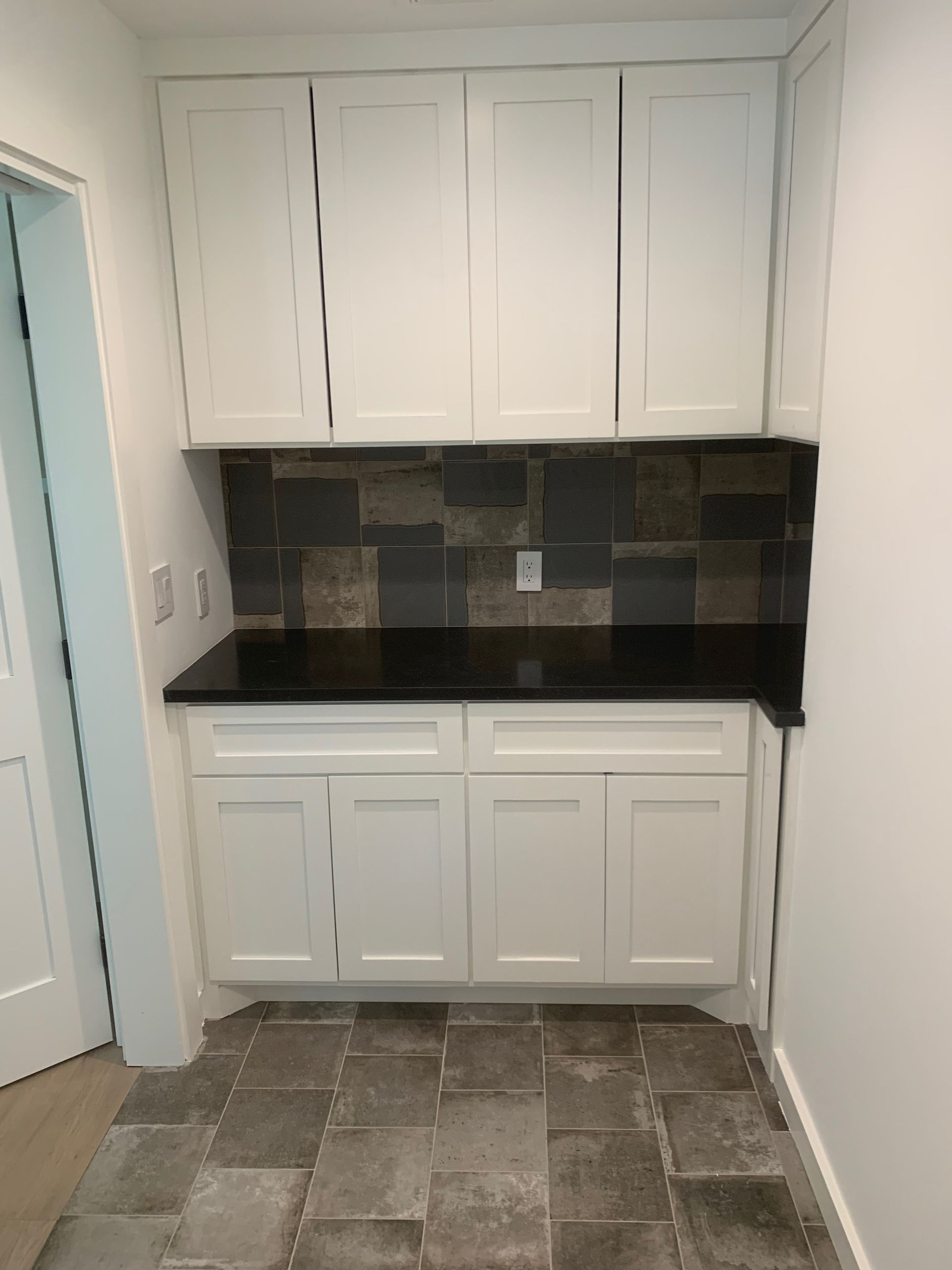 A kitchen with white cabinets and black counter tops.