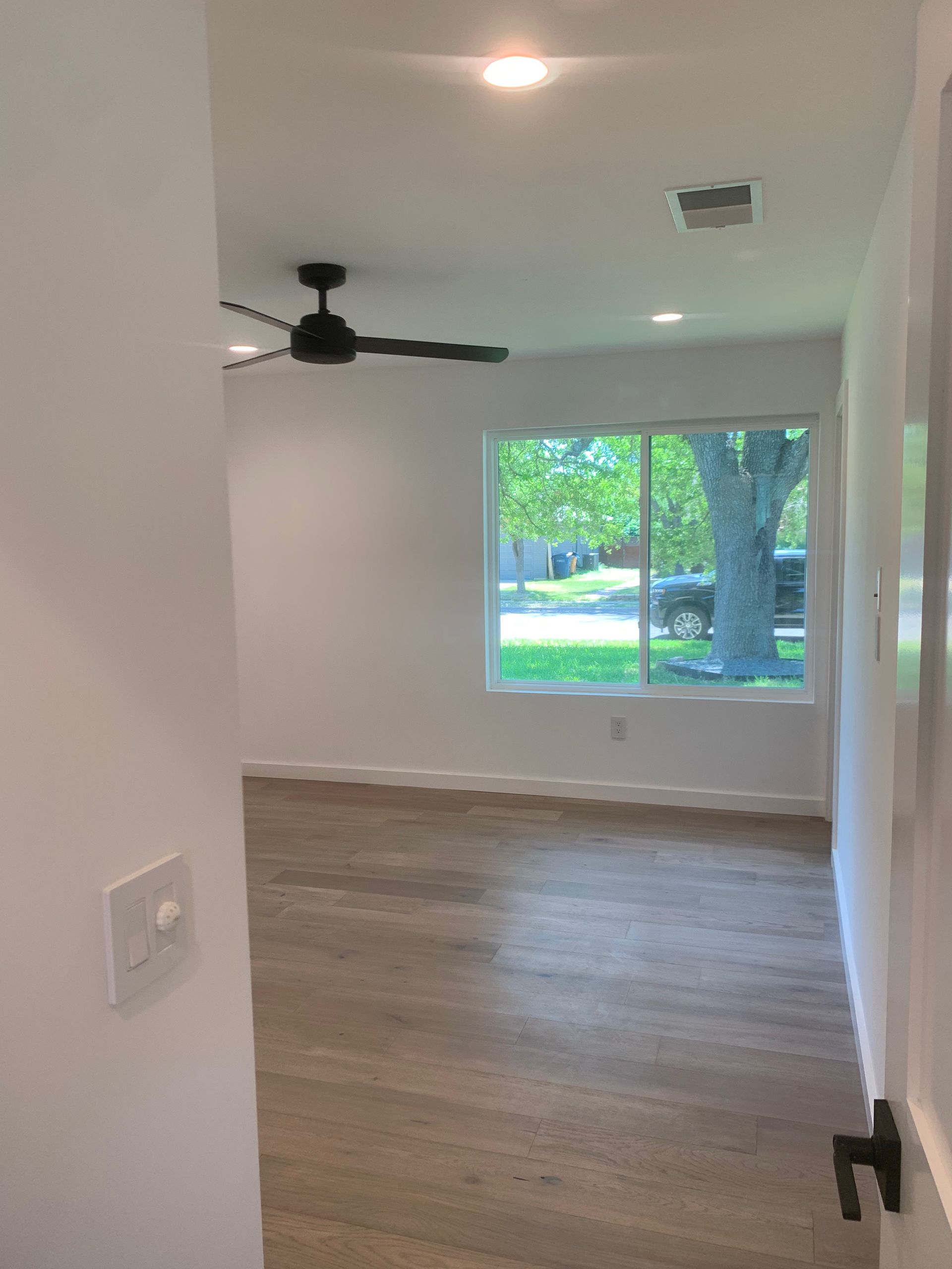 An empty room with a ceiling fan and a large window.
