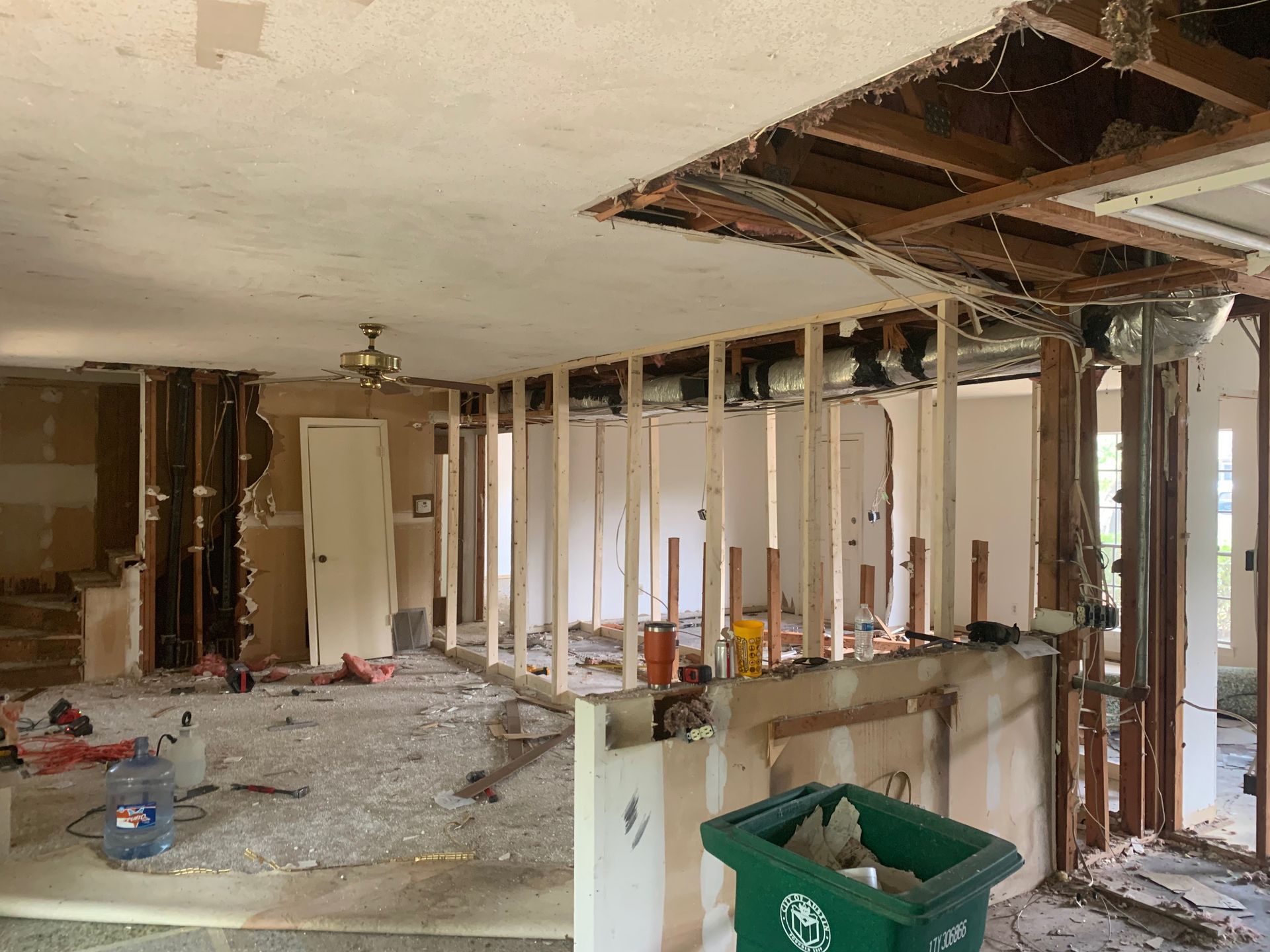 A green trash can is in the middle of a room under construction.