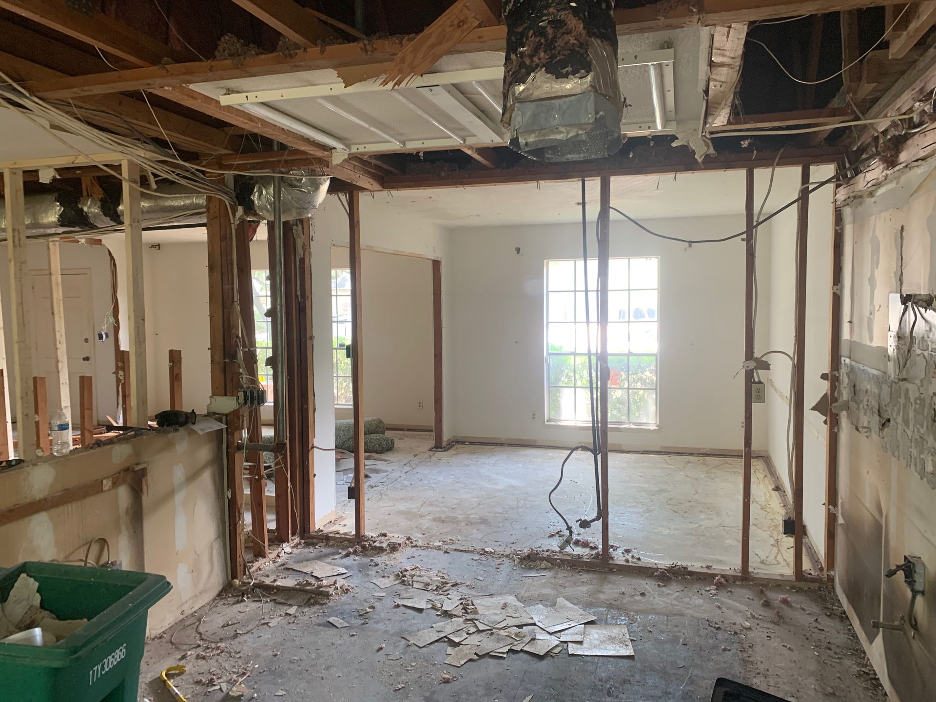 An empty room with a green trash can in the middle of it.