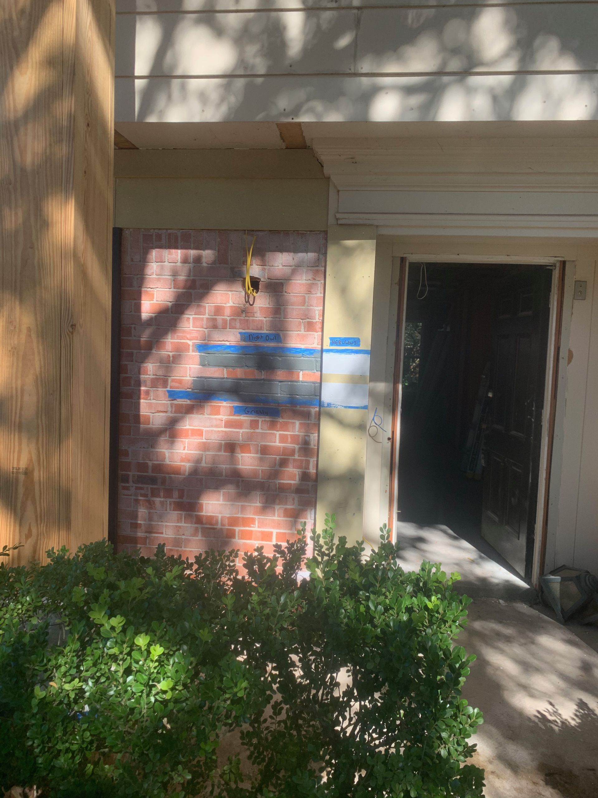 A brick building with a door and a bush in front of it.