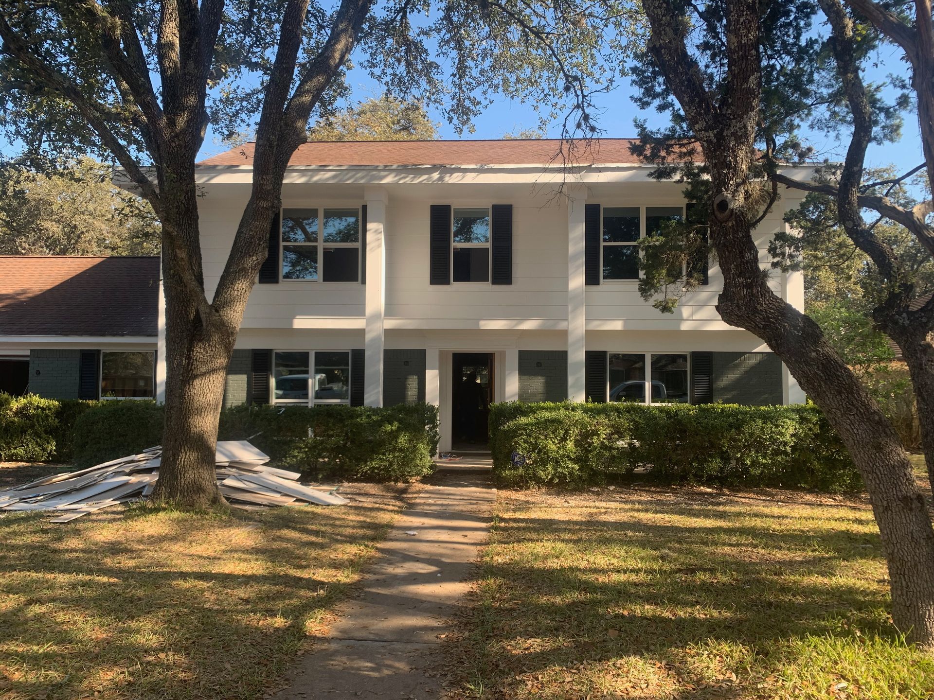 A white house with black shutters is surrounded by trees and grass.