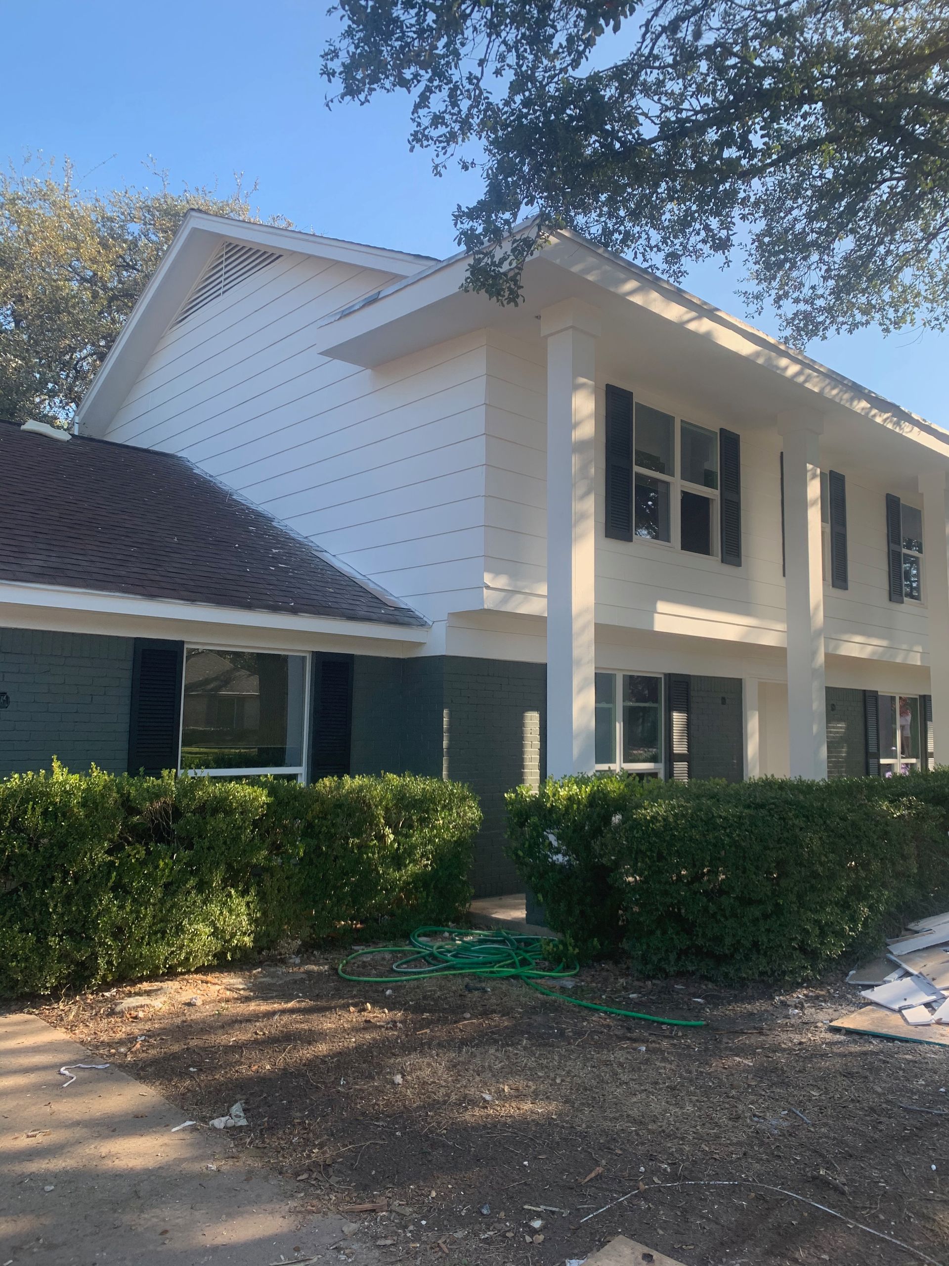 A large white house with black shutters and a tree in the background.