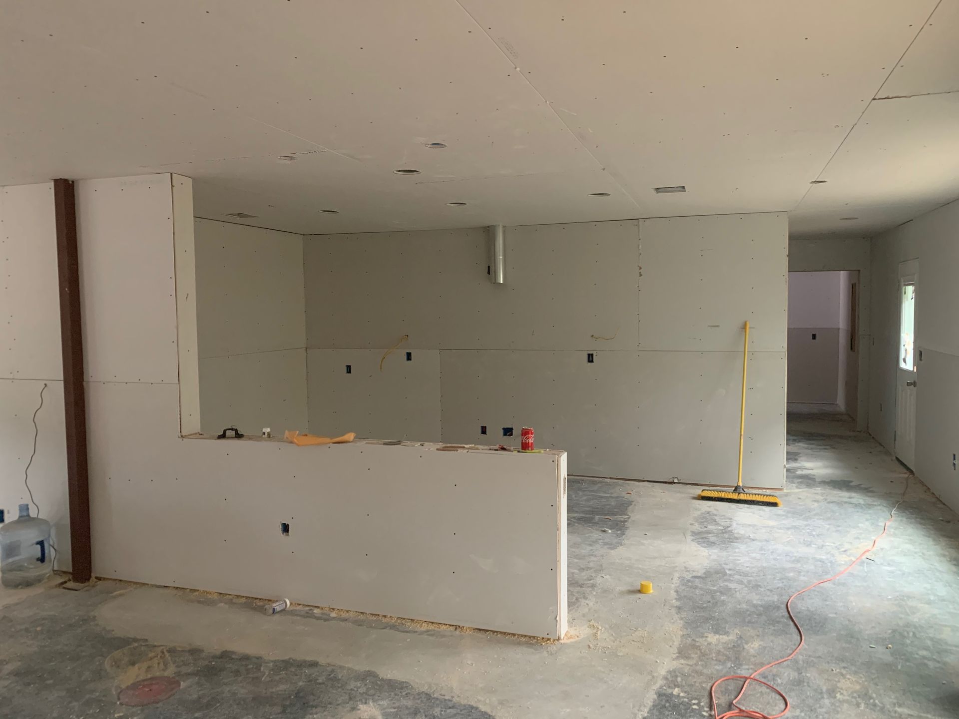 A large room with drywall walls and a broom on the floor.