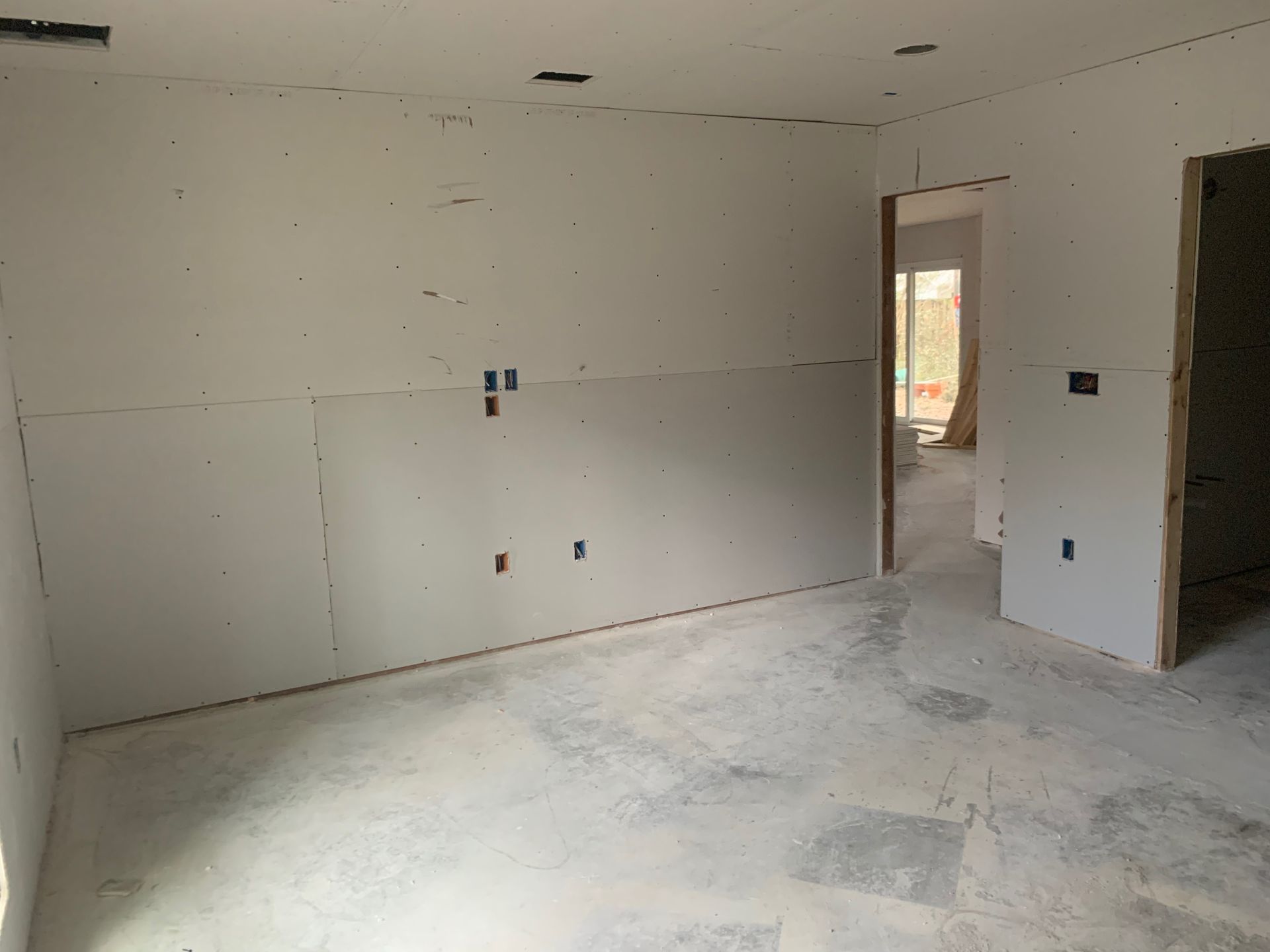 An empty room with drywall on the walls and a doorway leading to another room.