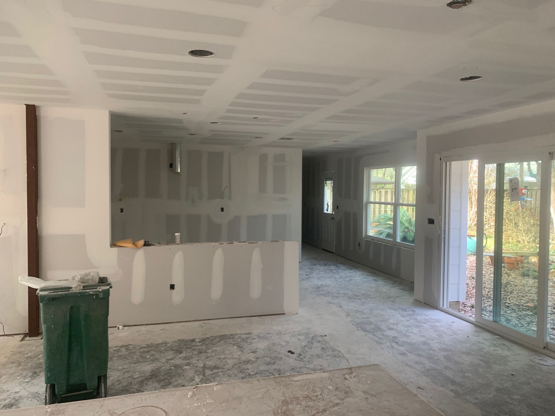 A large empty room with a green trash can in the middle of it.