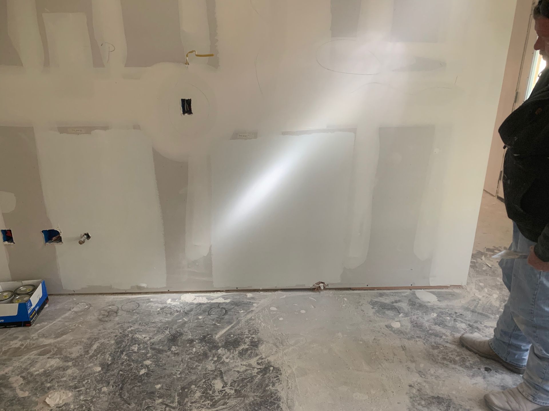 A man is standing in front of a drywall wall in a room.