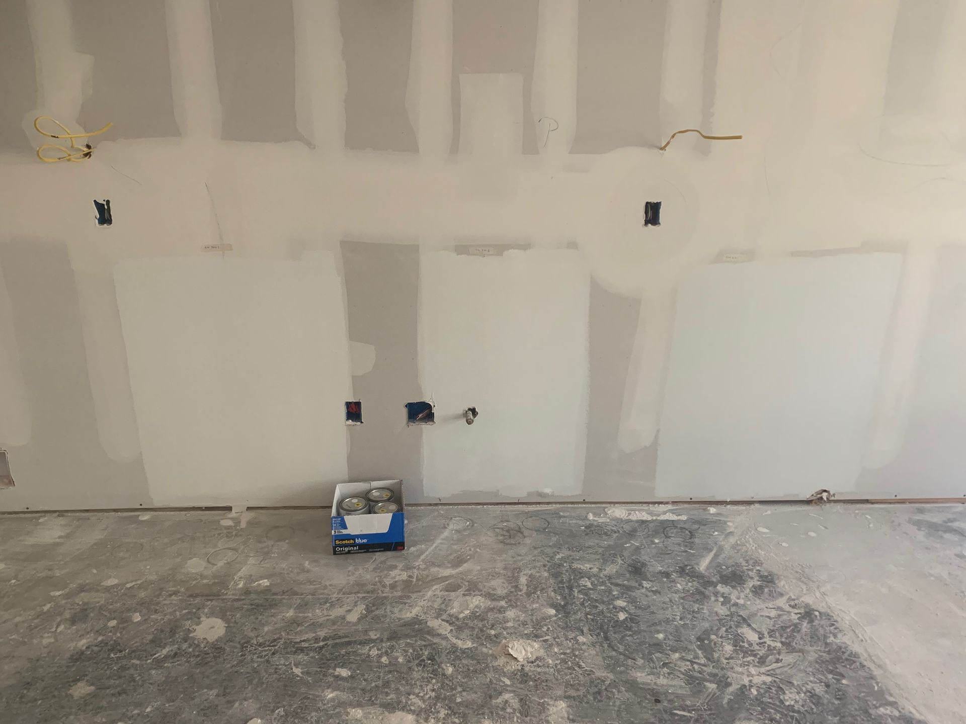 A box of paint is sitting on the floor in front of a drywall wall.