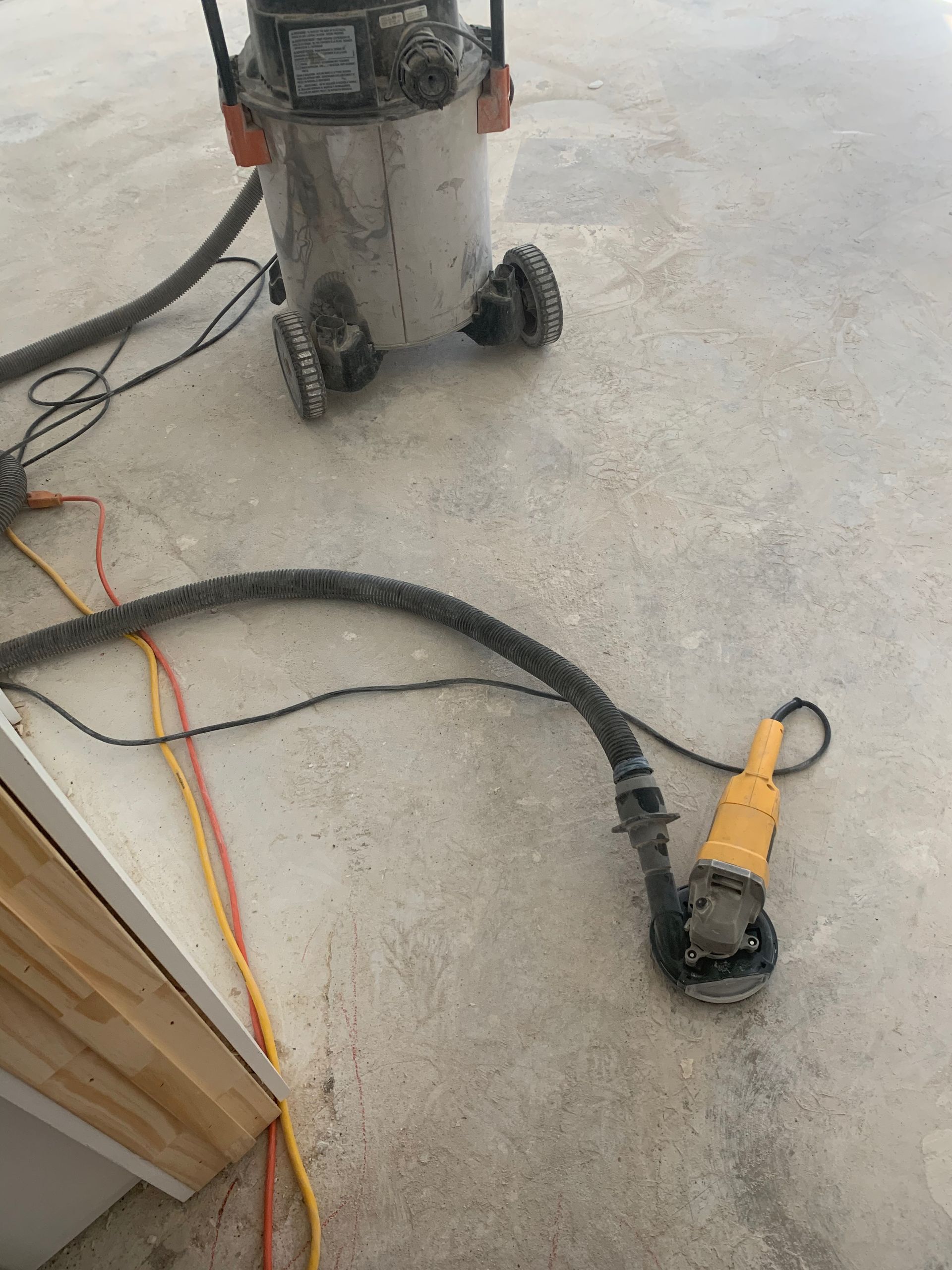 A vacuum cleaner is sitting on the floor next to a grinder.