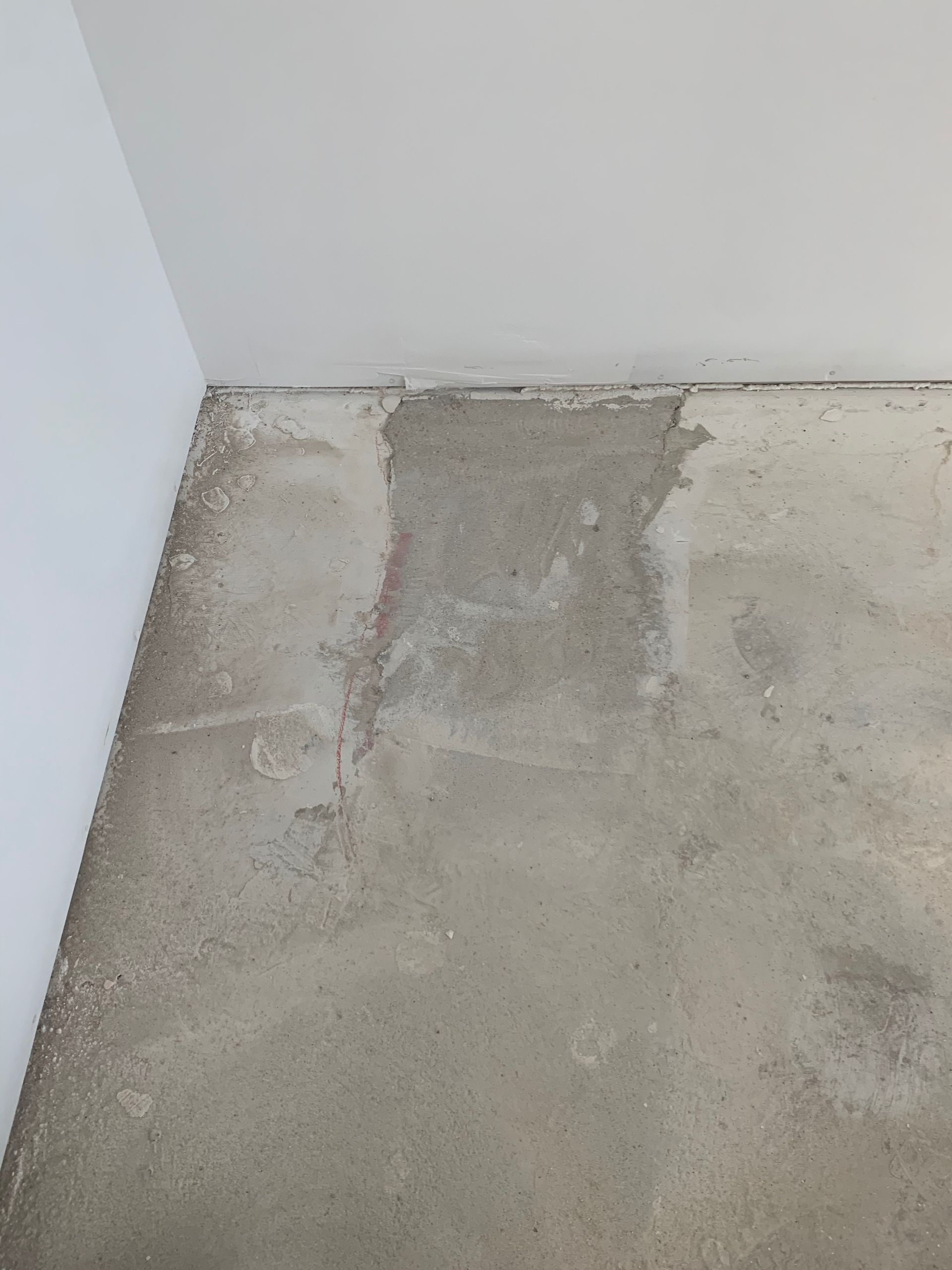 A corner of a room with a concrete floor and a white wall.