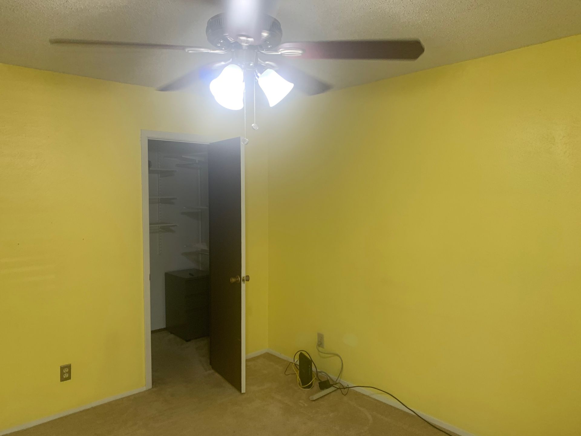 An empty room with yellow walls and a ceiling fan.