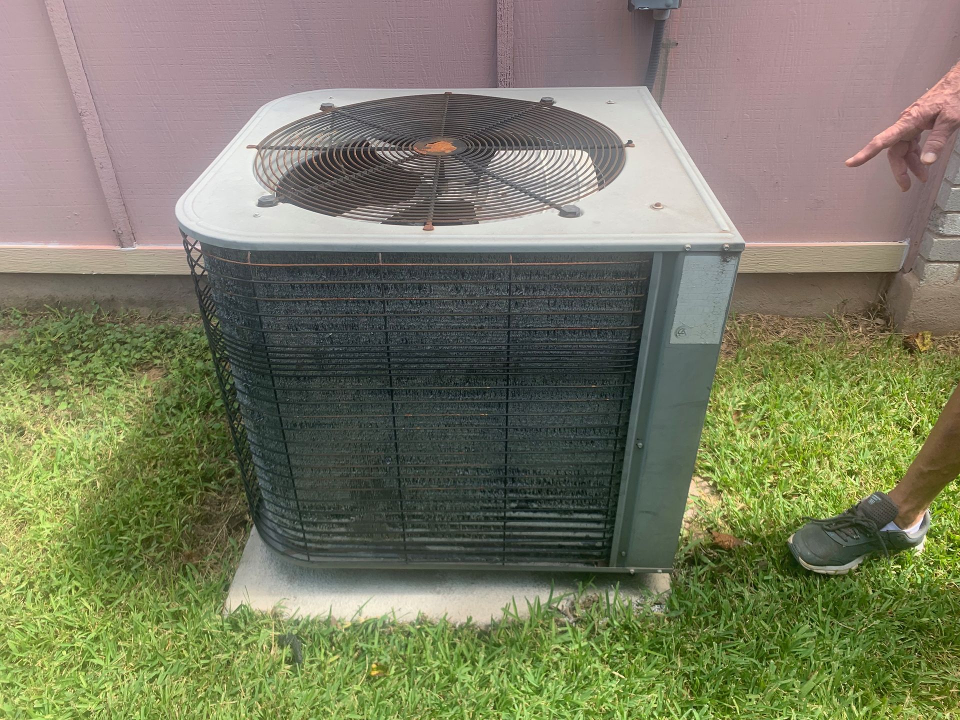 A person is standing next to a large air conditioner in the grass.