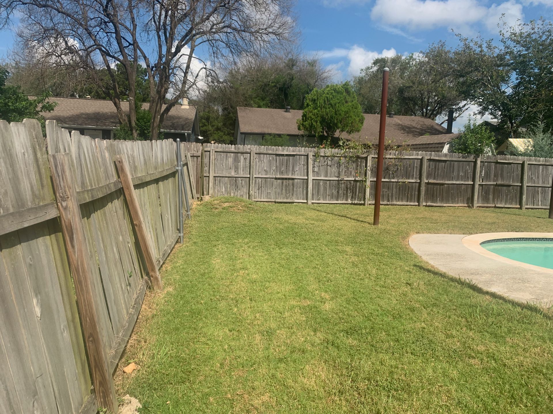 A wooden fence surrounds a swimming pool in a backyard.