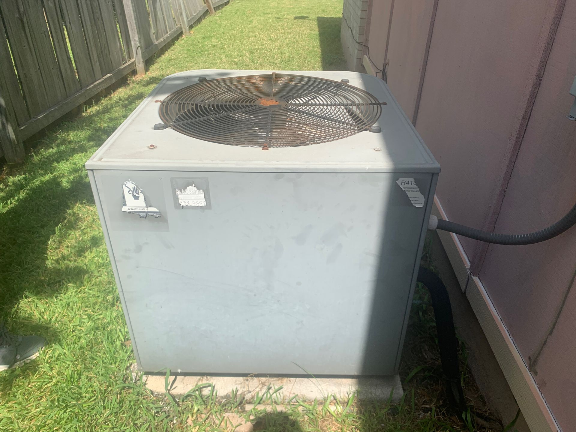 An air conditioner is sitting in the grass next to a building.