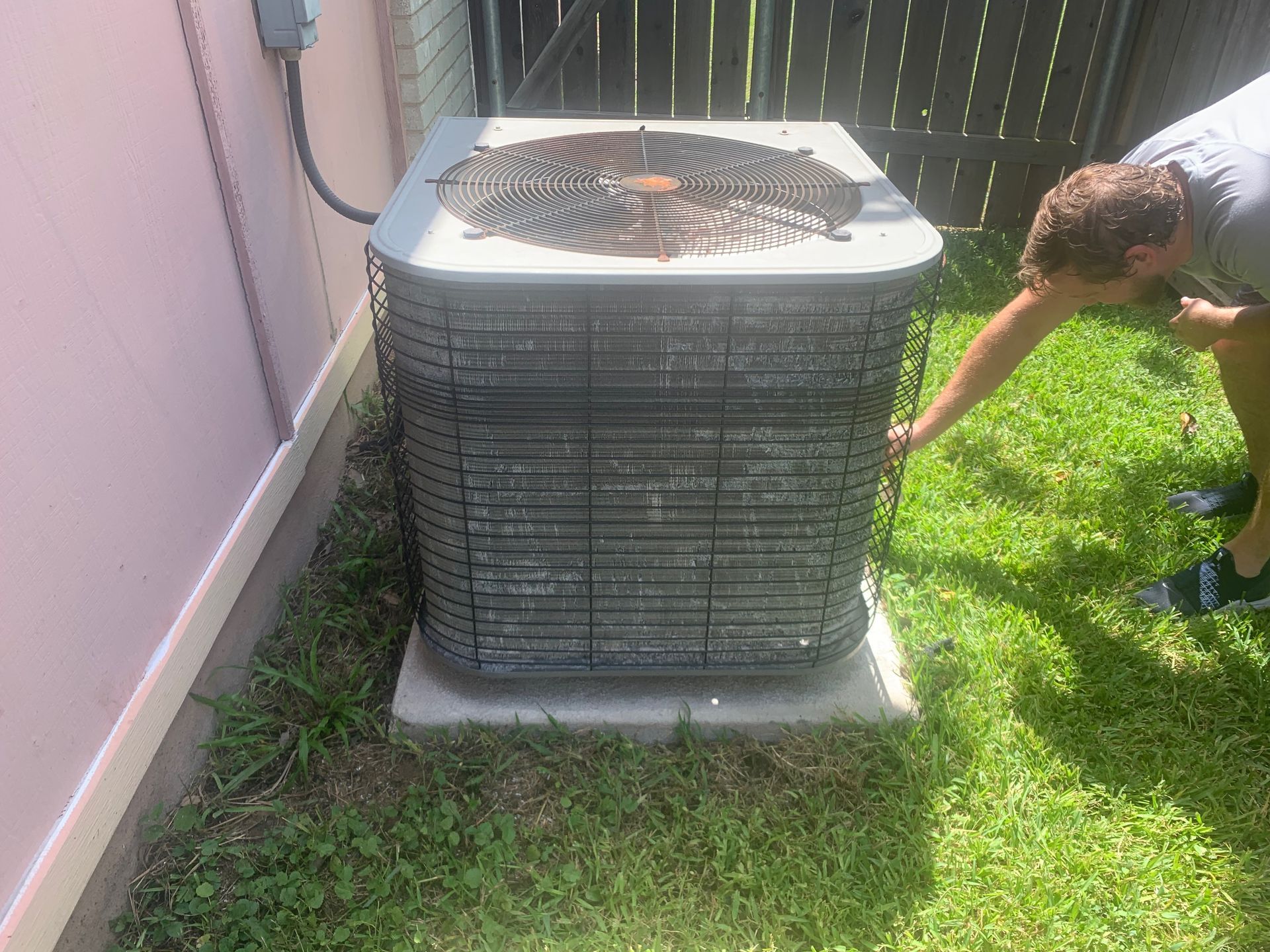 A man is looking at an air conditioner in the grass.