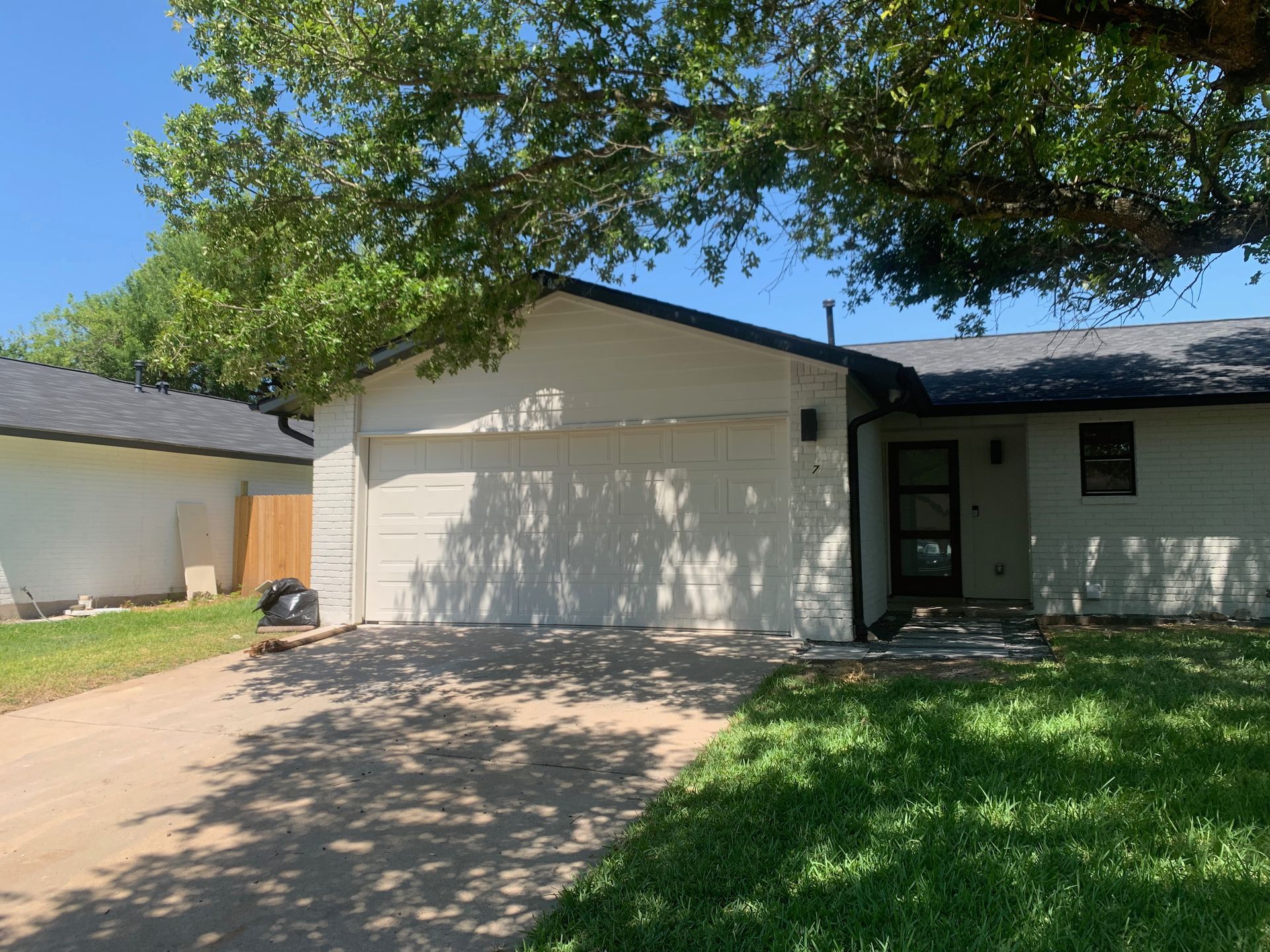 A white house with a black roof and a tree in front of it.