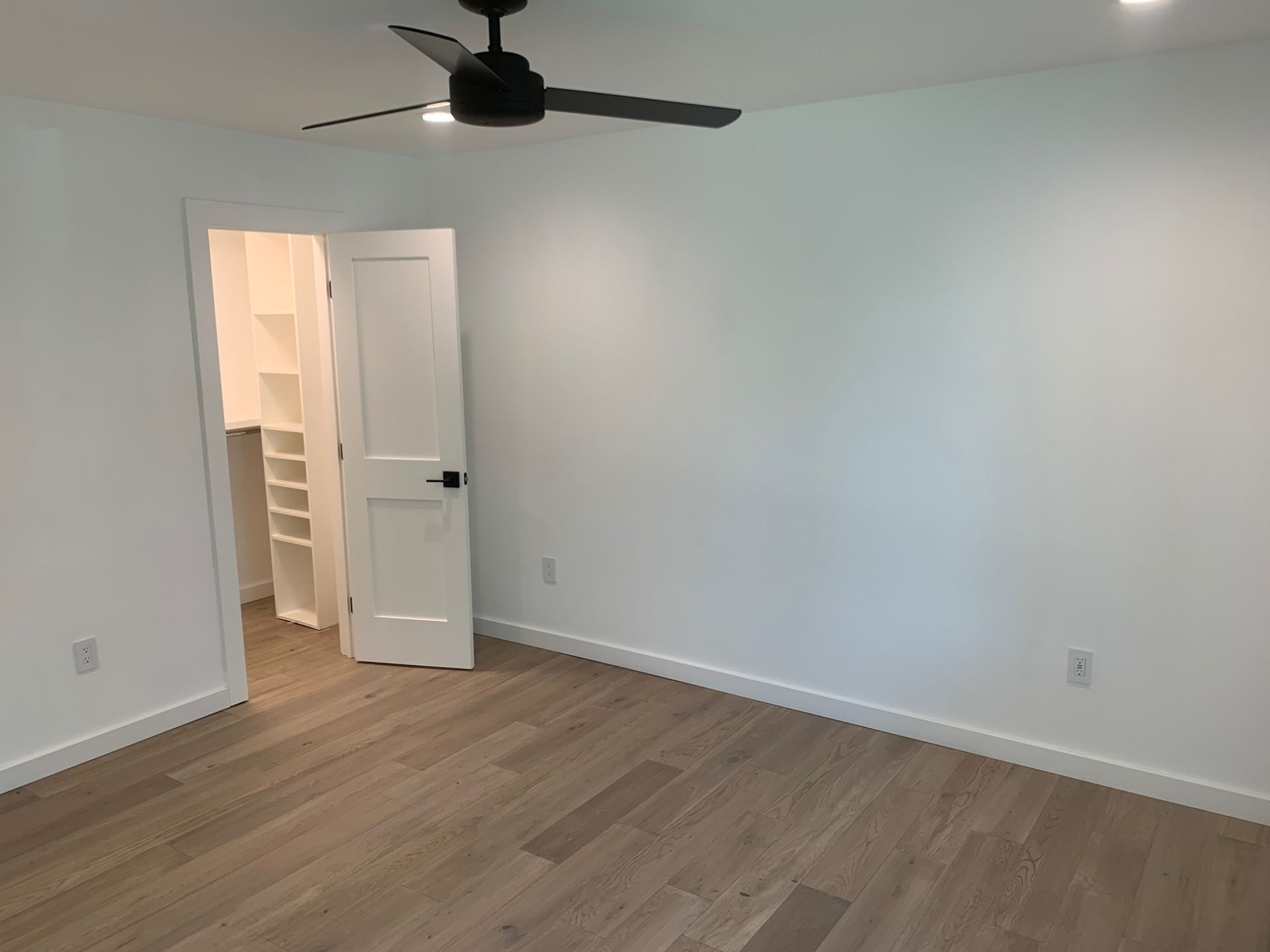 An empty bedroom with hardwood floors and a ceiling fan.