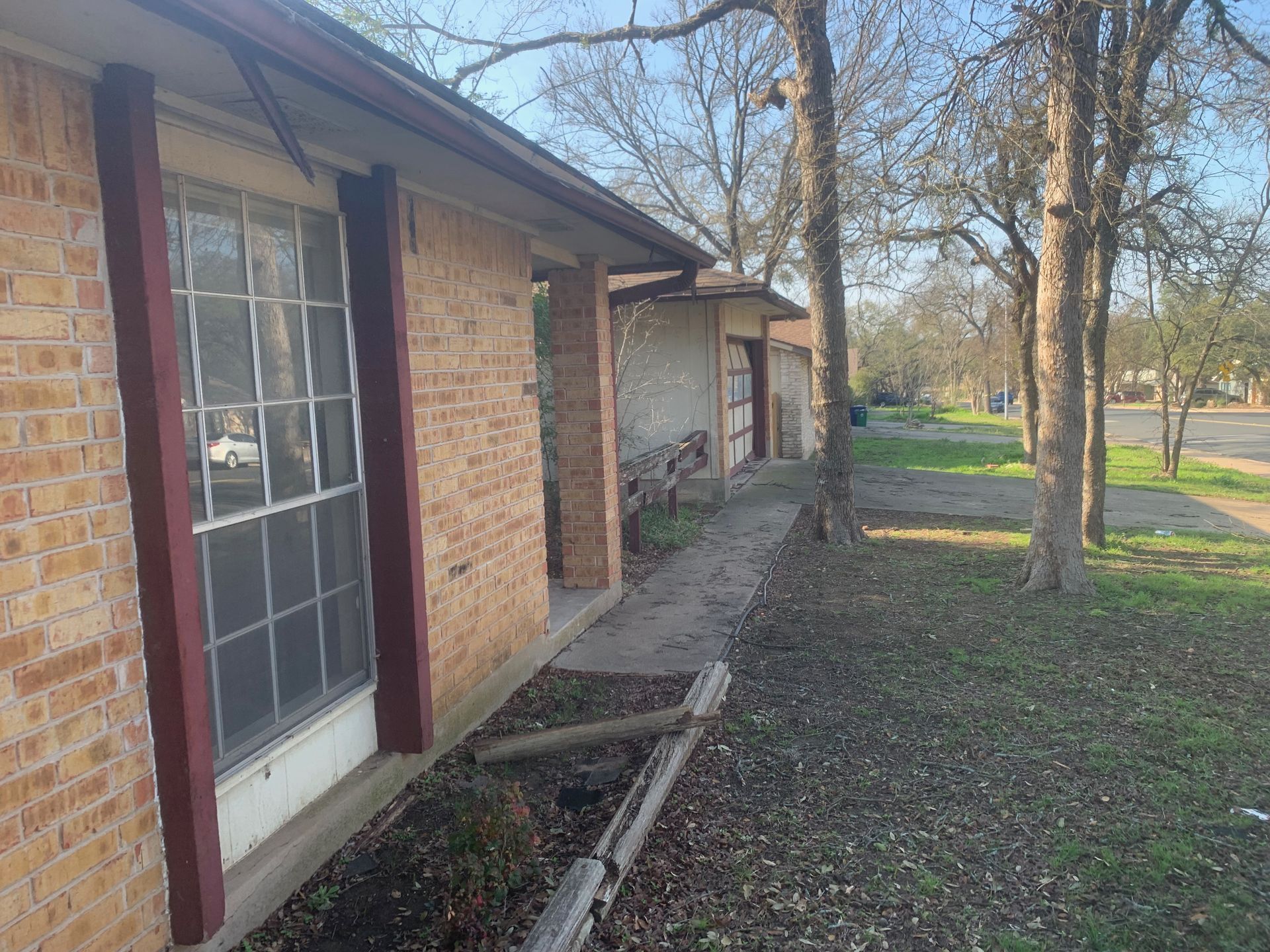 A brick house with a sidewalk and trees in front of it.