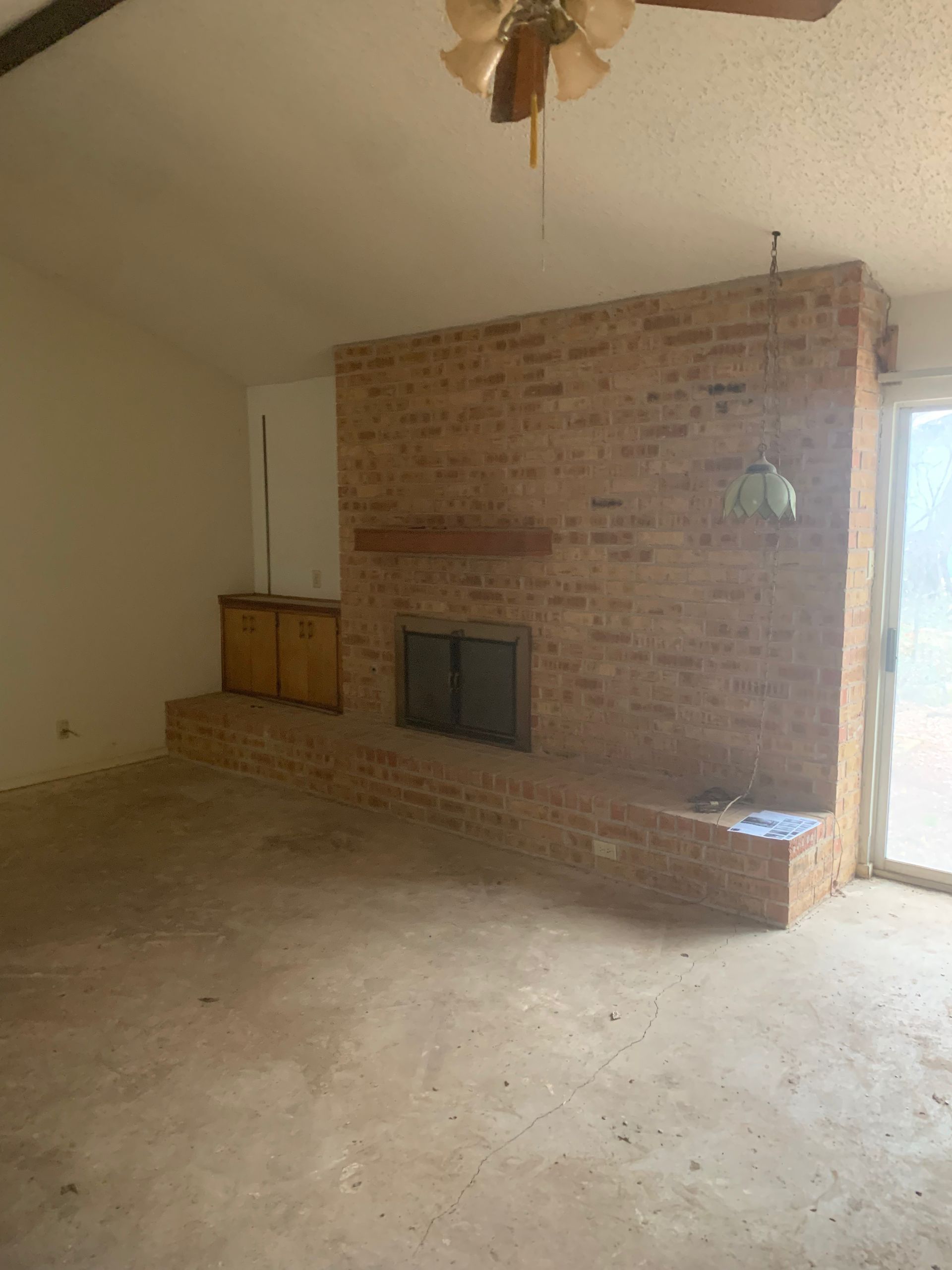 An empty living room with a brick fireplace and a ceiling fan.