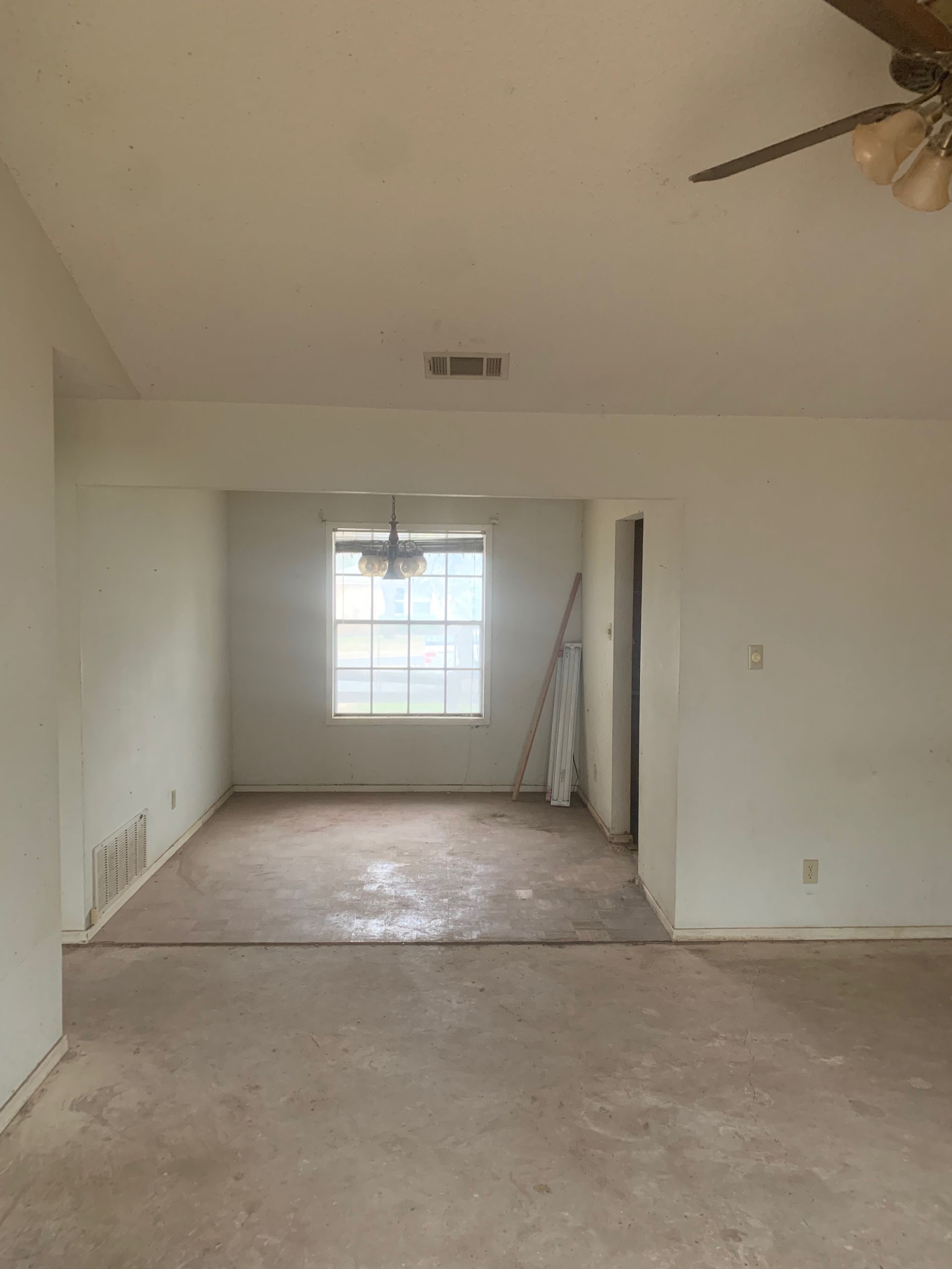 An empty living room with a ceiling fan and a window.