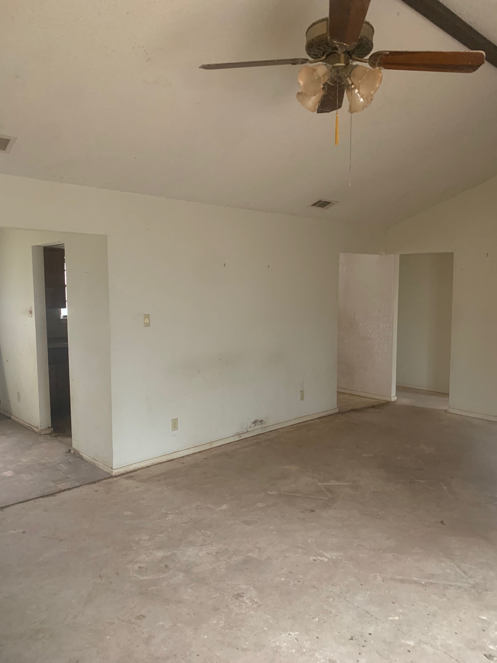 An empty living room with a ceiling fan hanging from the ceiling.