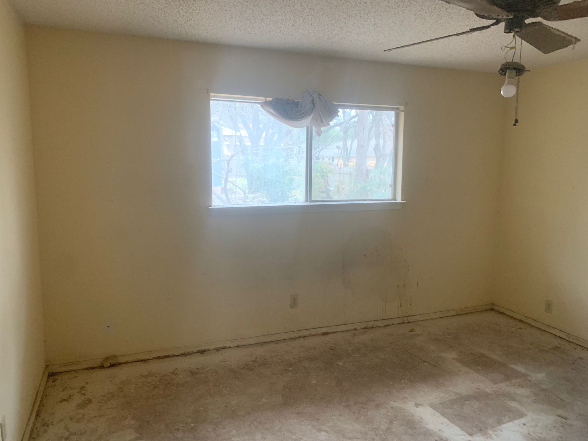 An empty room with a ceiling fan and a window.