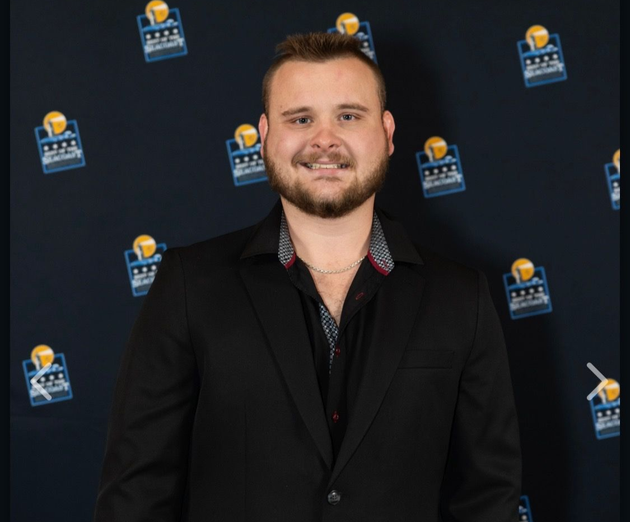 Man in a black suit posing on a step-and-repeat backdrop at a formal event