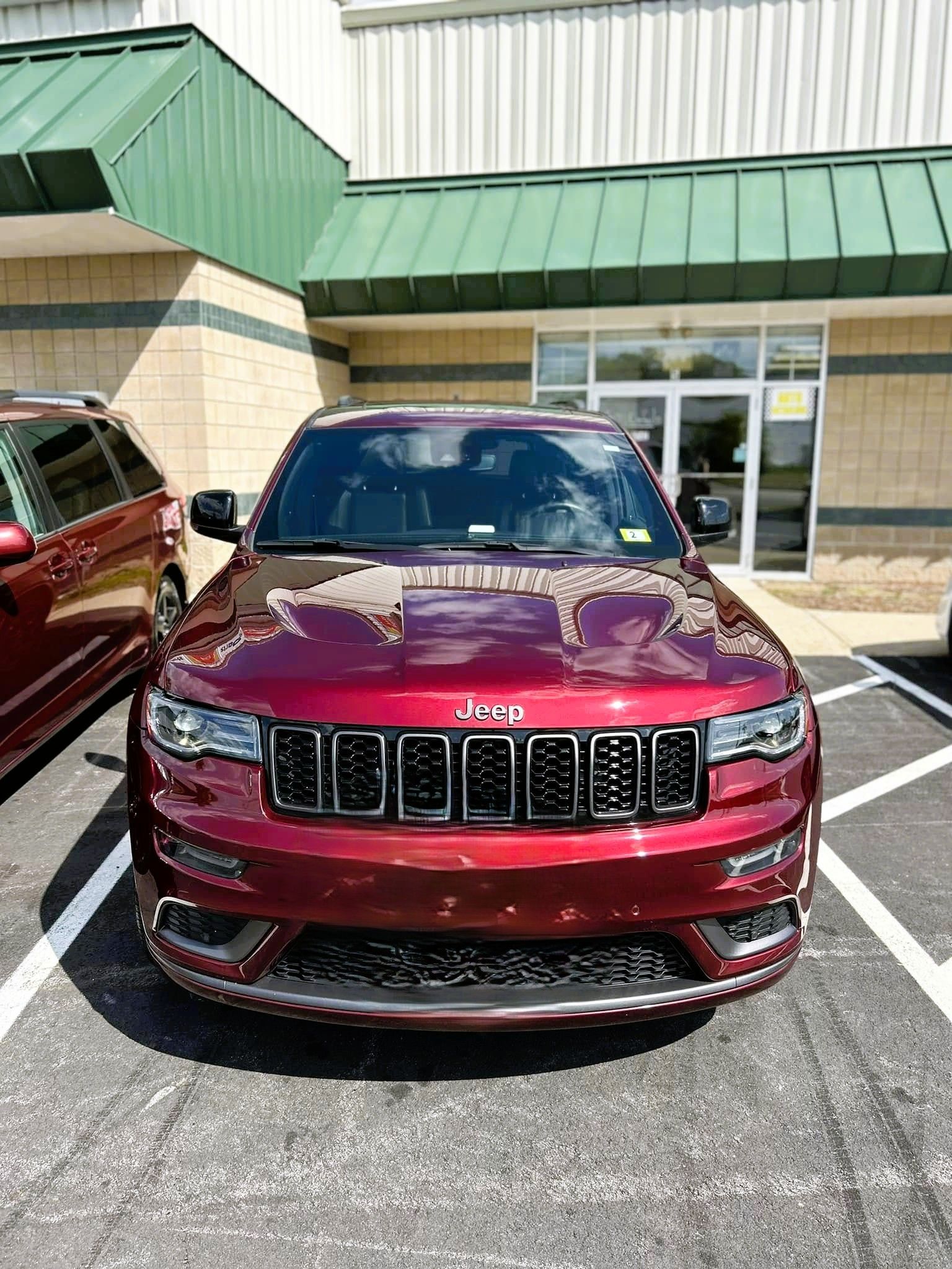 Maroon Jeep SUV parked in front of a storefront with green awning and glass doors.