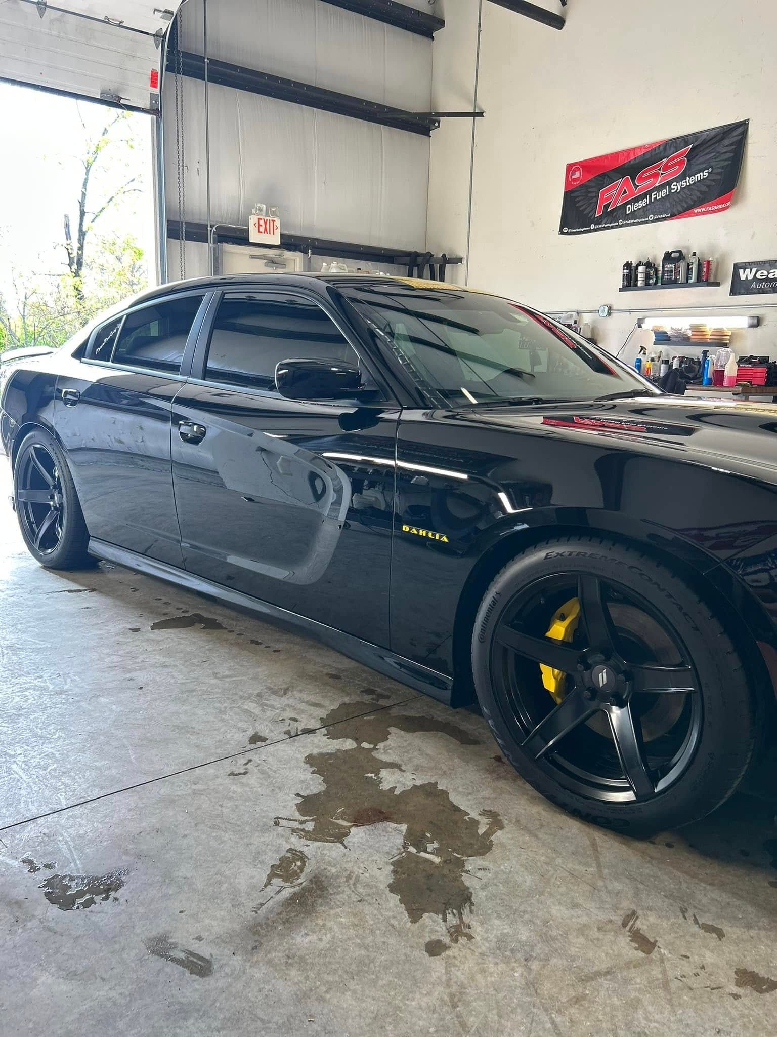 Black sports sedan with yellow brake calipers parked inside an auto shop.