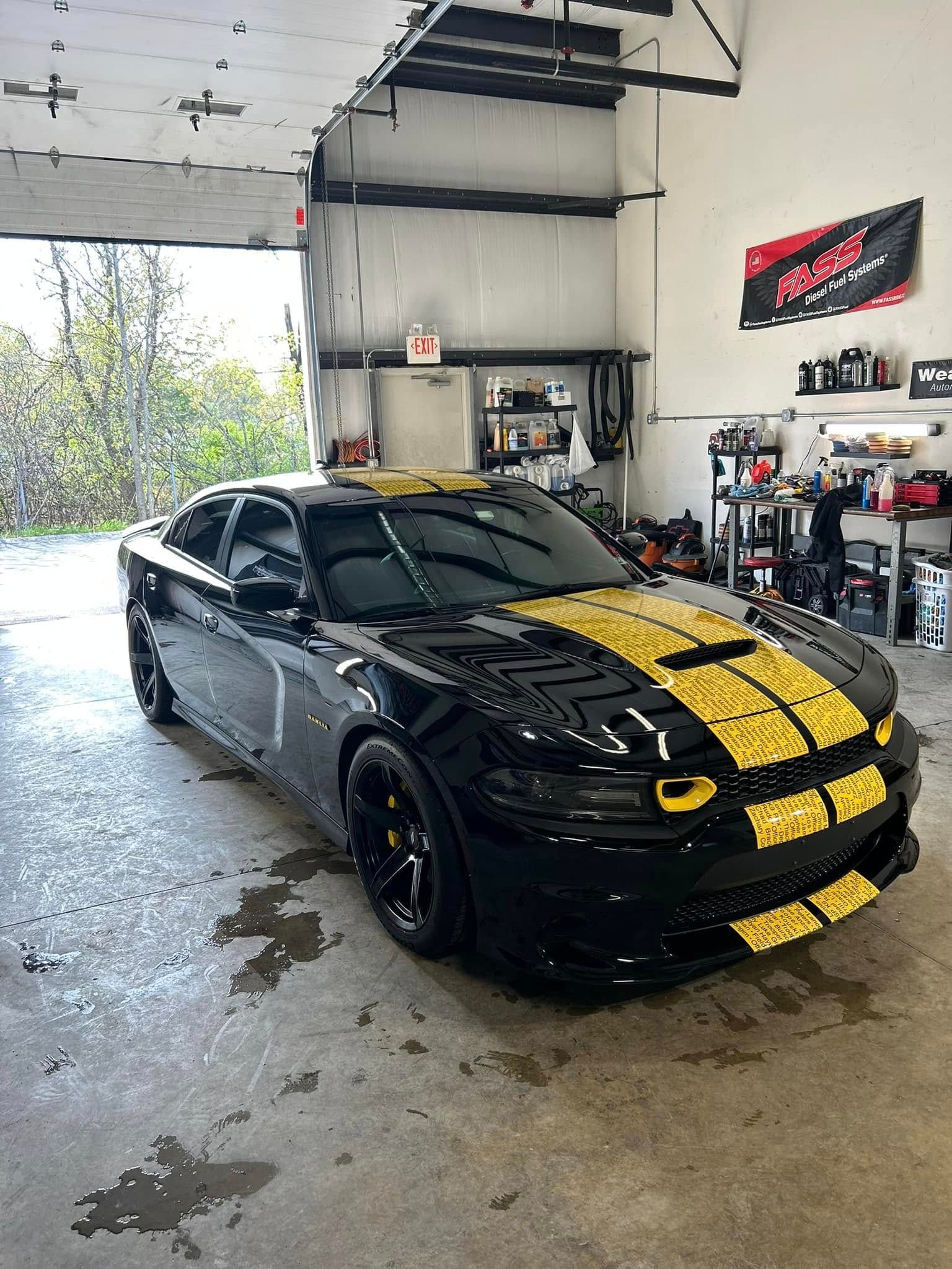 Black sports car with yellow racing stripes parked inside a garage.