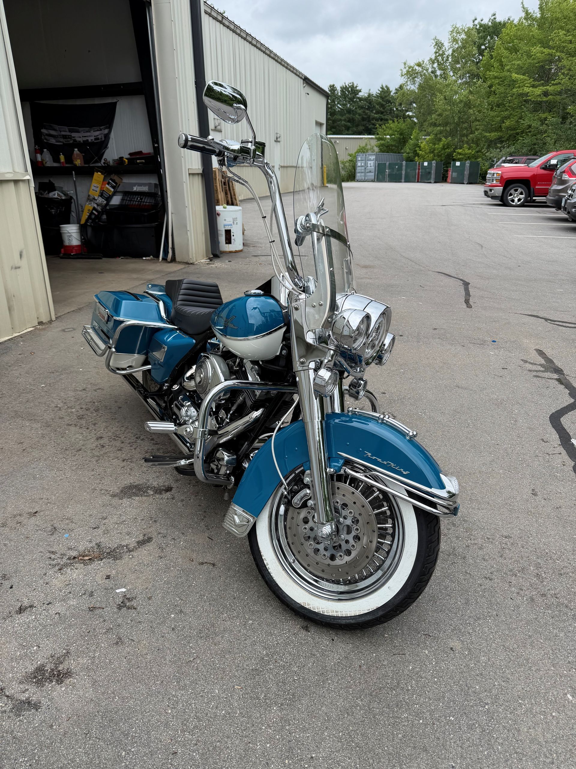 Blue-and-chrome cruiser motorcycle parked beside a garage in an industrial lot
