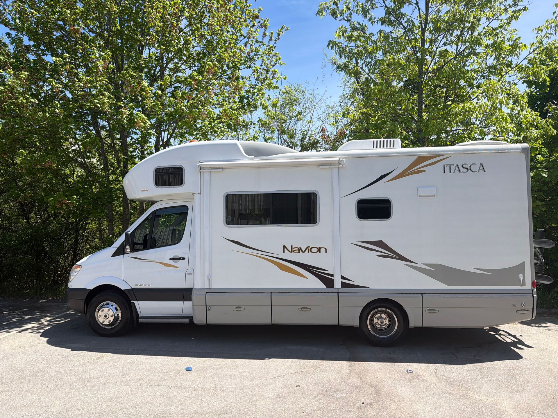 White motorhome parked on a sunny roadside with trees in the background