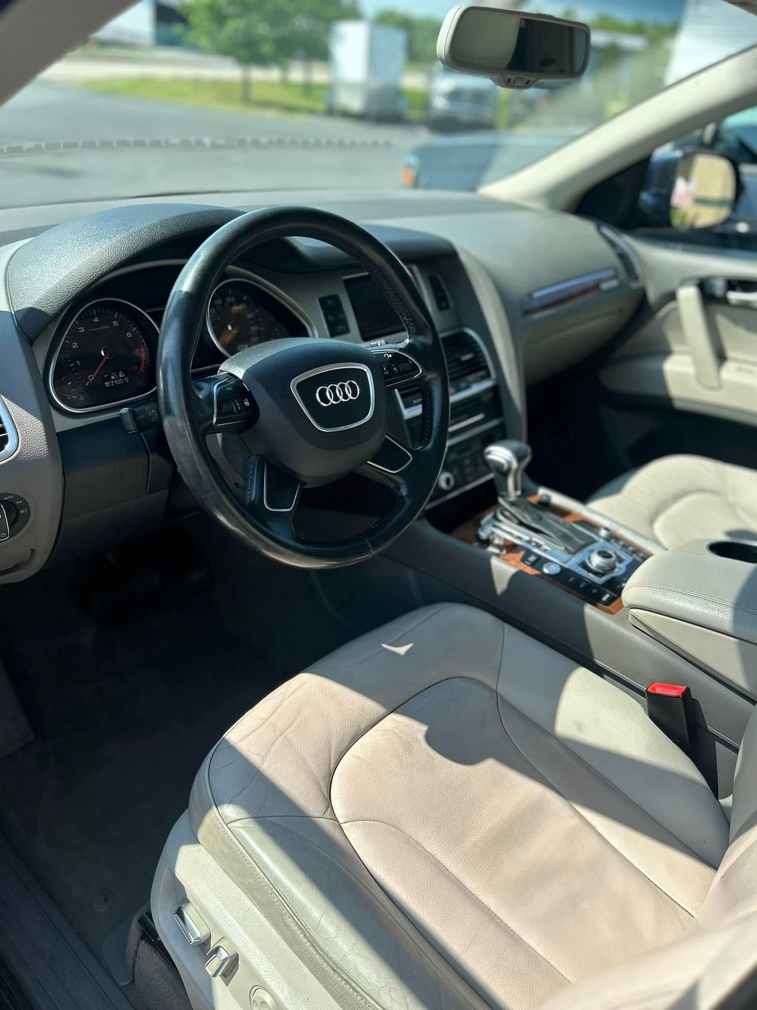 Car interior with black leather steering wheel, beige seats, and center console in sunlight
