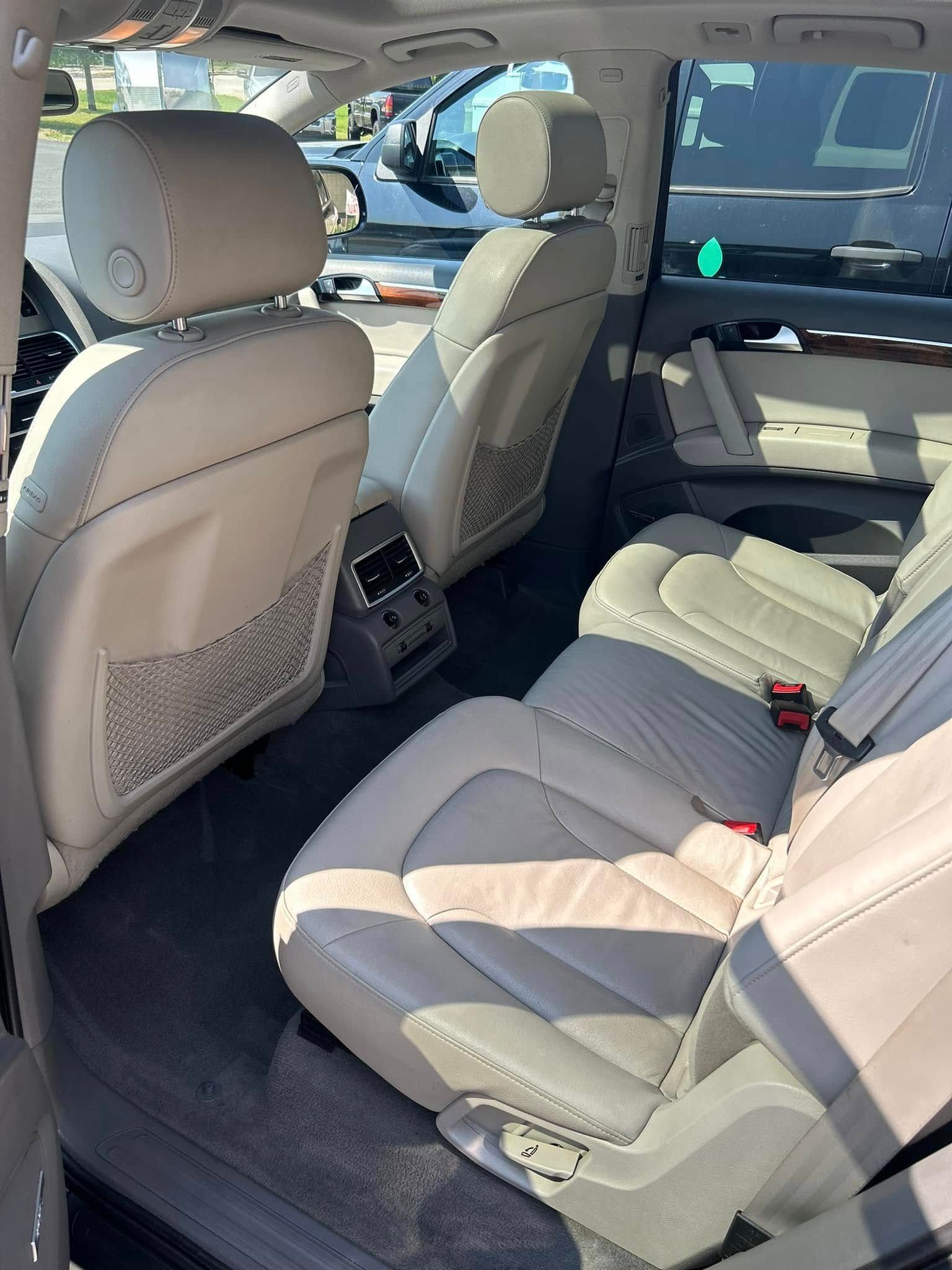 Interior of a beige car, showing front and rear seats and the center console from the back seat.